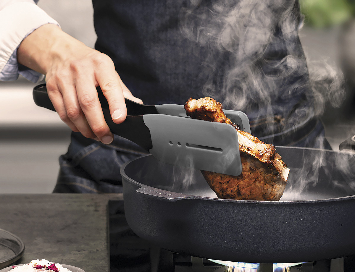 Cook it Küchenzange Ein dampfendes, angebratenes Stück Fleisch wird mithilfe der grauen Cock it Küchenzange in der heißen Pfanne gewendet.