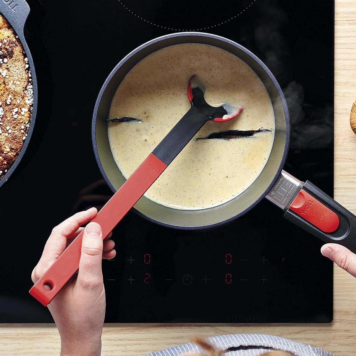 In einem runden Diamond Lite Stieltopf wird Vanillesauce gekocht und mit einem roten Cock it Lochlöffel umgerührt.