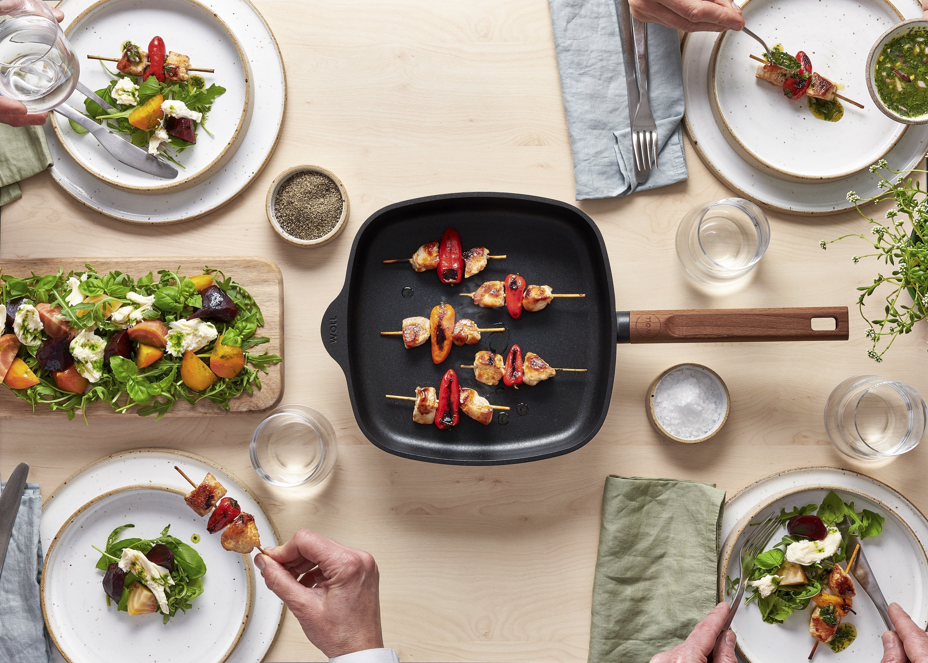 Auf dem Tisch steht eine viereckige Eco Logic QXR Pfanne, in der sich angebratene Fleischspieße befinden.