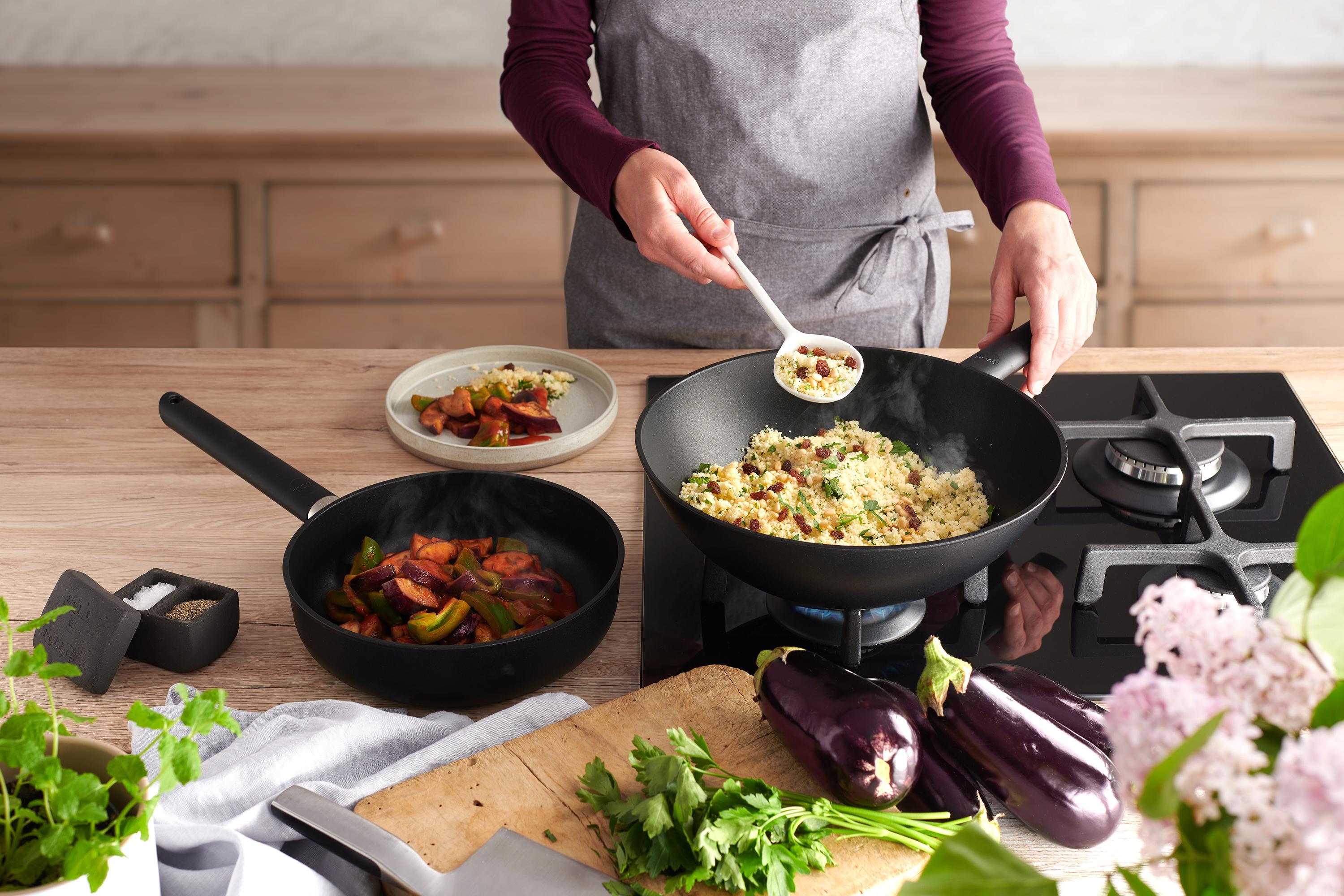 Eco Lite QXR Wok In einer runden Eco Lite QXR Wok- und Rührpfanne wird Couscous Salat zubereitet. Daneben steht eine weitere Eco Lite QXR Pfanne mit Gemüse.