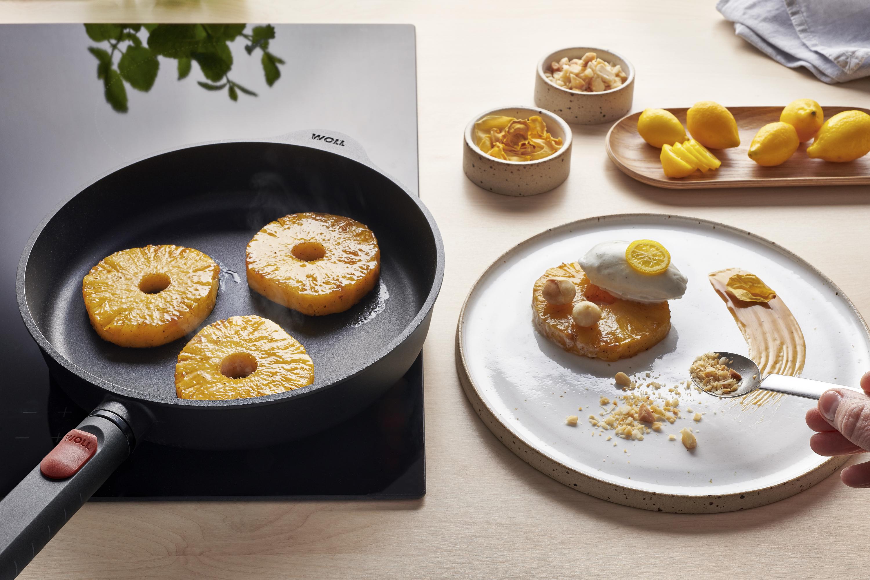 In einer runden Eco Logic QXR Pfanne werden Ananasscheiben angebraten und auf einem Teller mit Karamellsauce und Eis angerichtet.