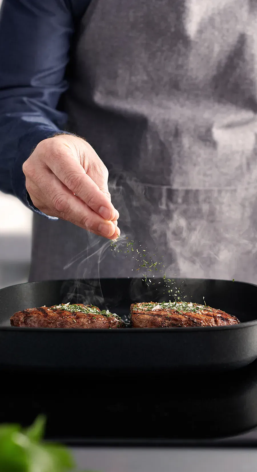 Auf dem Herd steht die rechteckige, heiße Logic-Grillpfanne, in der saftig angebratenes Fleisch dampft. Es ist mit Kräutersalz bestreut.
