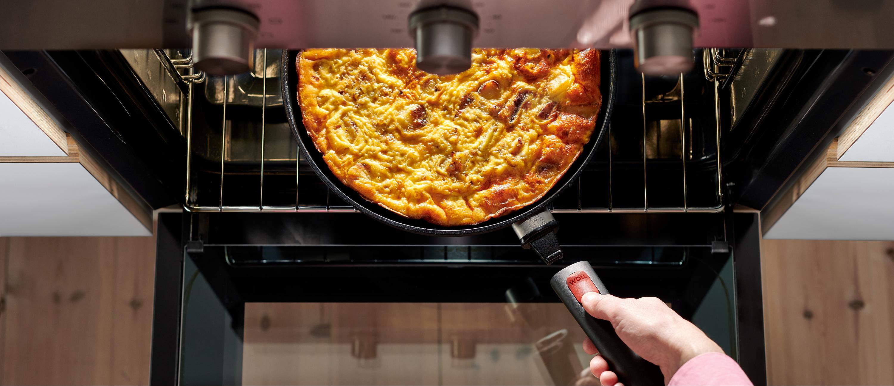 Eine runde, heiße Pfanne der Serie Eco Lite QXR steht mit einem dampfenden Gericht auf dem Rost des Backofens. Um die Pfanne aus dem Backofen zu nehmen, wird der abnehmbare Stiel wieder eingerastet.