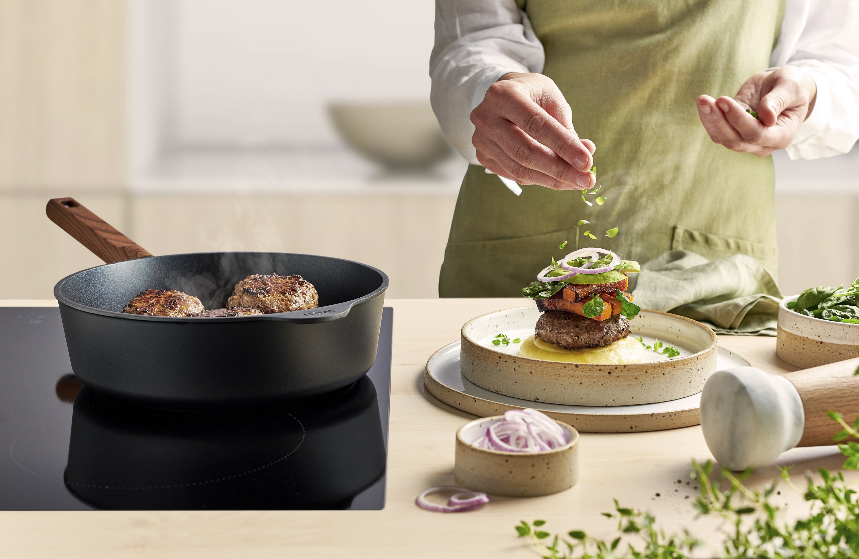 Eco Logic QXR Guss-Hochrandpfanne In einer runden Eco Logic QXR Pfanne werden Frikadellen angebraten und auf einem Teller platziert.