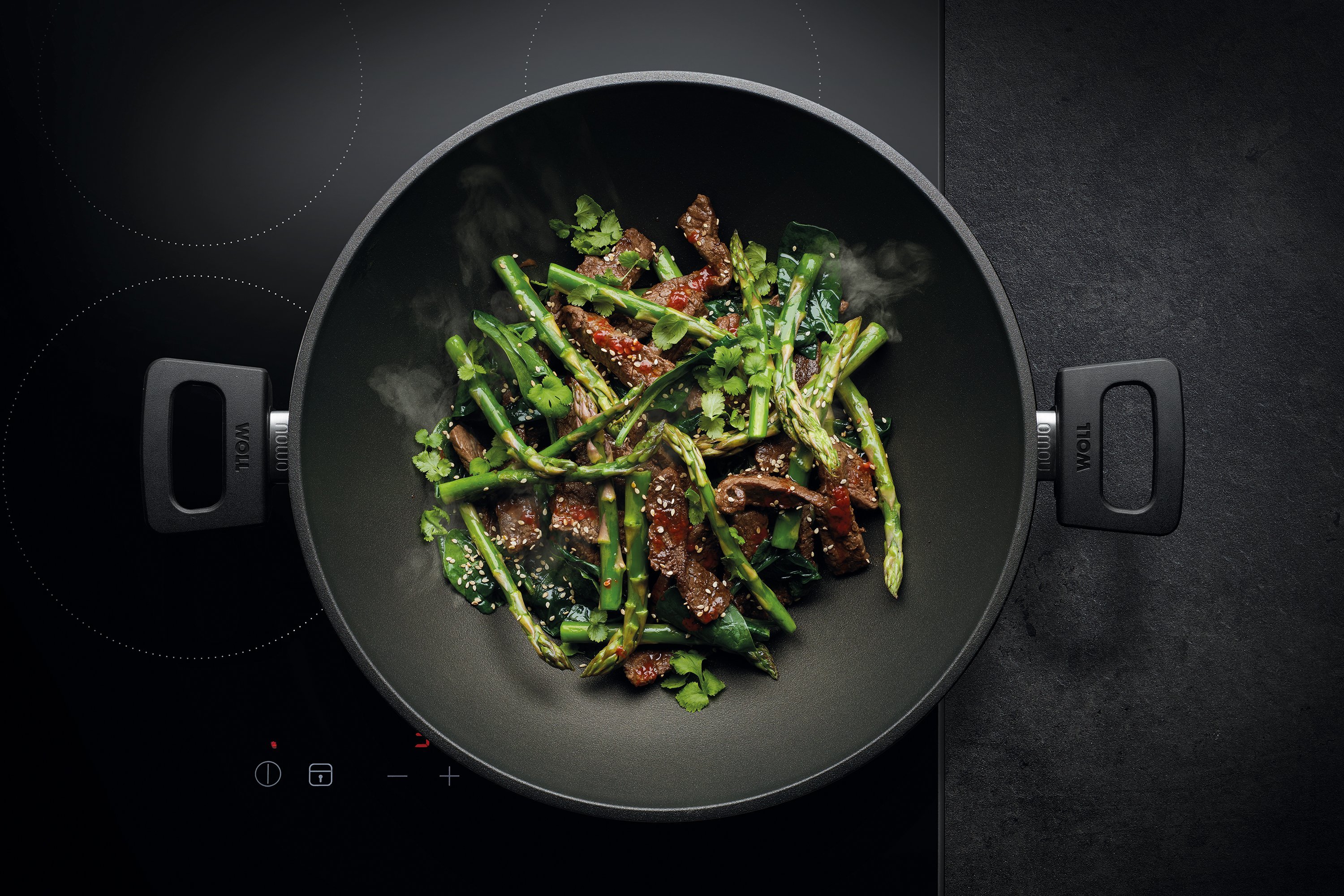 Auf dem Herd steht ein runder, heißer Wok der Serie Nowo. Darin befindet sich frisch angebratenes Rindfleisch mit Spargel.