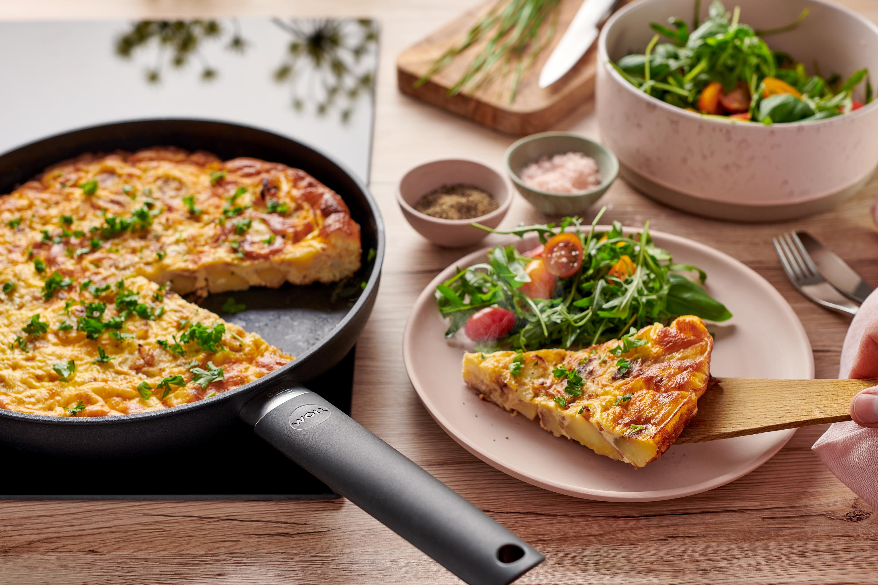 Eco Lite QXR Flachpfanne In einer runden Eco Lite QXR Pfanne befindet sich eine frische spanische Tortilla. Ein Stück davon liegt dem Teller.