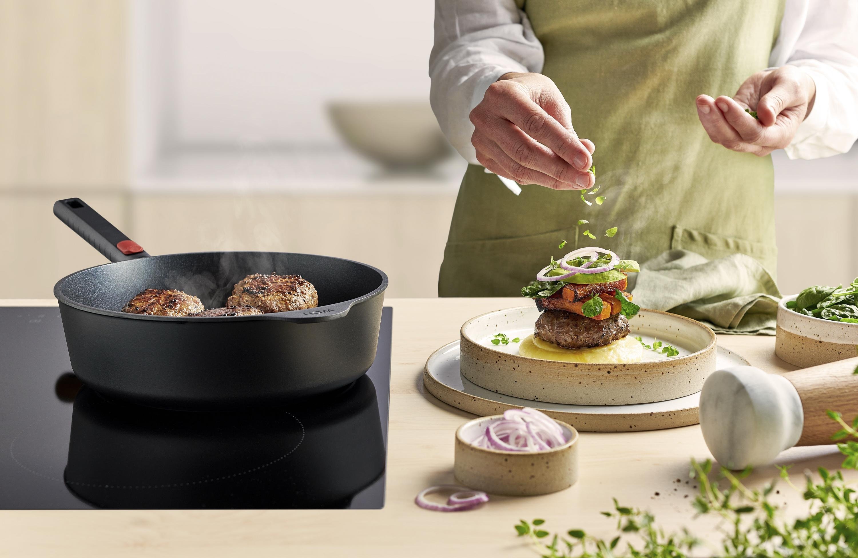 Eco Logic QXR Guss-Hochrandpfanne In einer runden Eco Logic QXR Pfanne werden Frikadellen angebraten und auf einem Teller platziert.