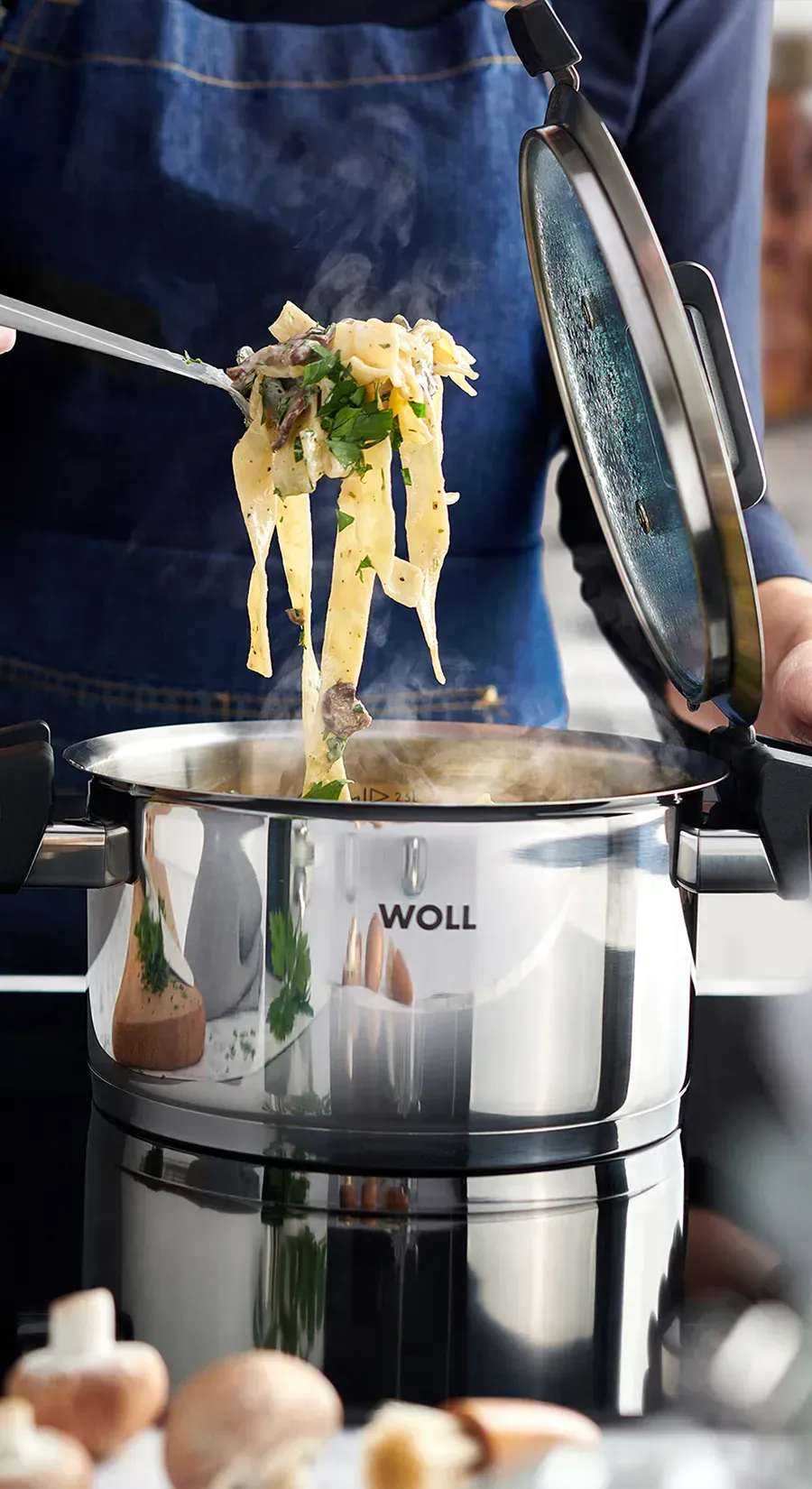 Im runden Edelstahltopf der Serie „Concept” befinden sich frisch zubereitete Bandnudeln. Der Deckel wurde abgenommen und in die dafür vorgesehene Halterung am Griff gesteckt. Im Vordergrund sieht man Pilze.