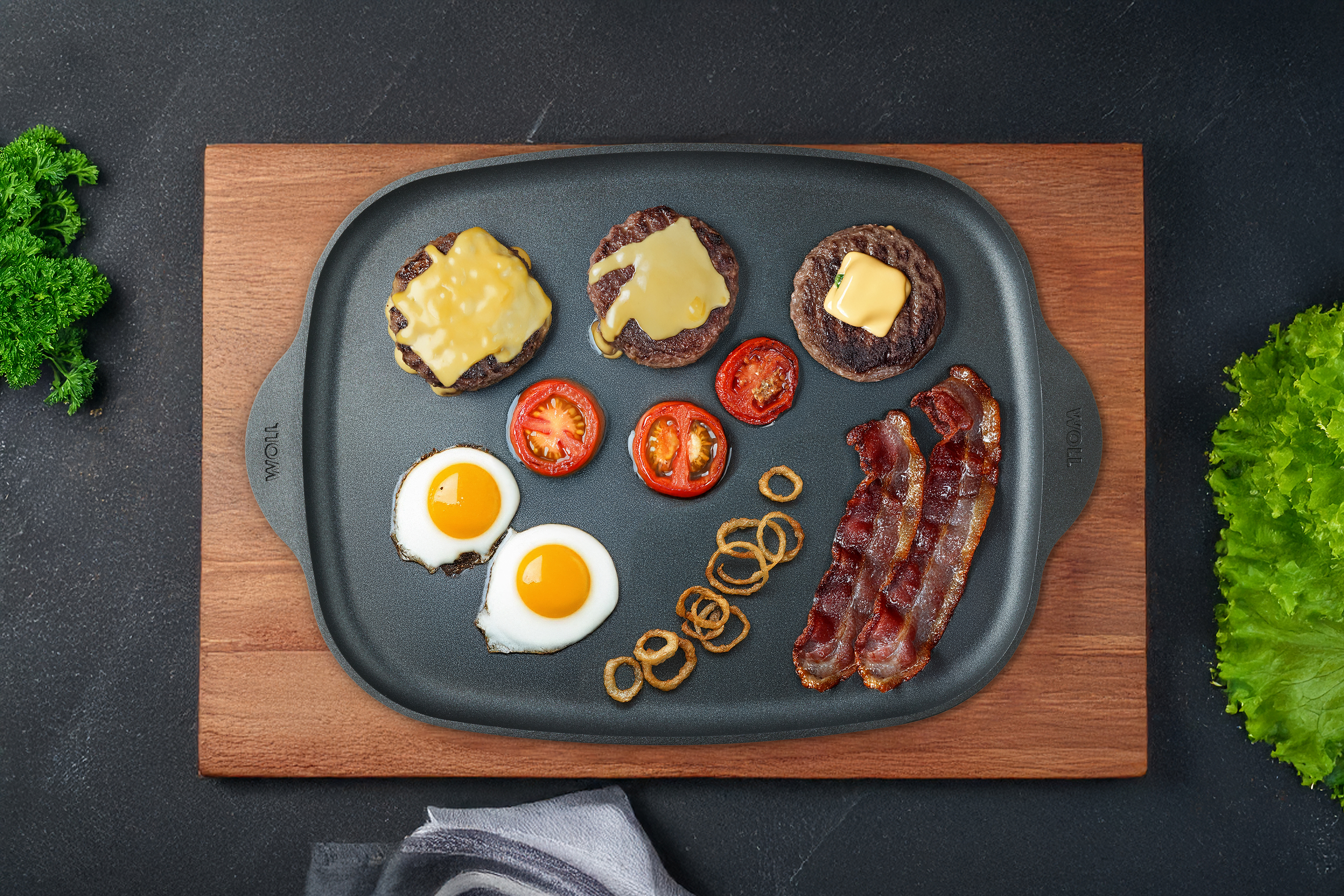 Eco Logic QXR Guss-Grillplatte / Teppan-Yaki-Platte Auf einer Eco Logic QXR Grillplatte liegen gebackene Spiegeleier, Burgerpattys, Bacon und Tomatenscheiben.