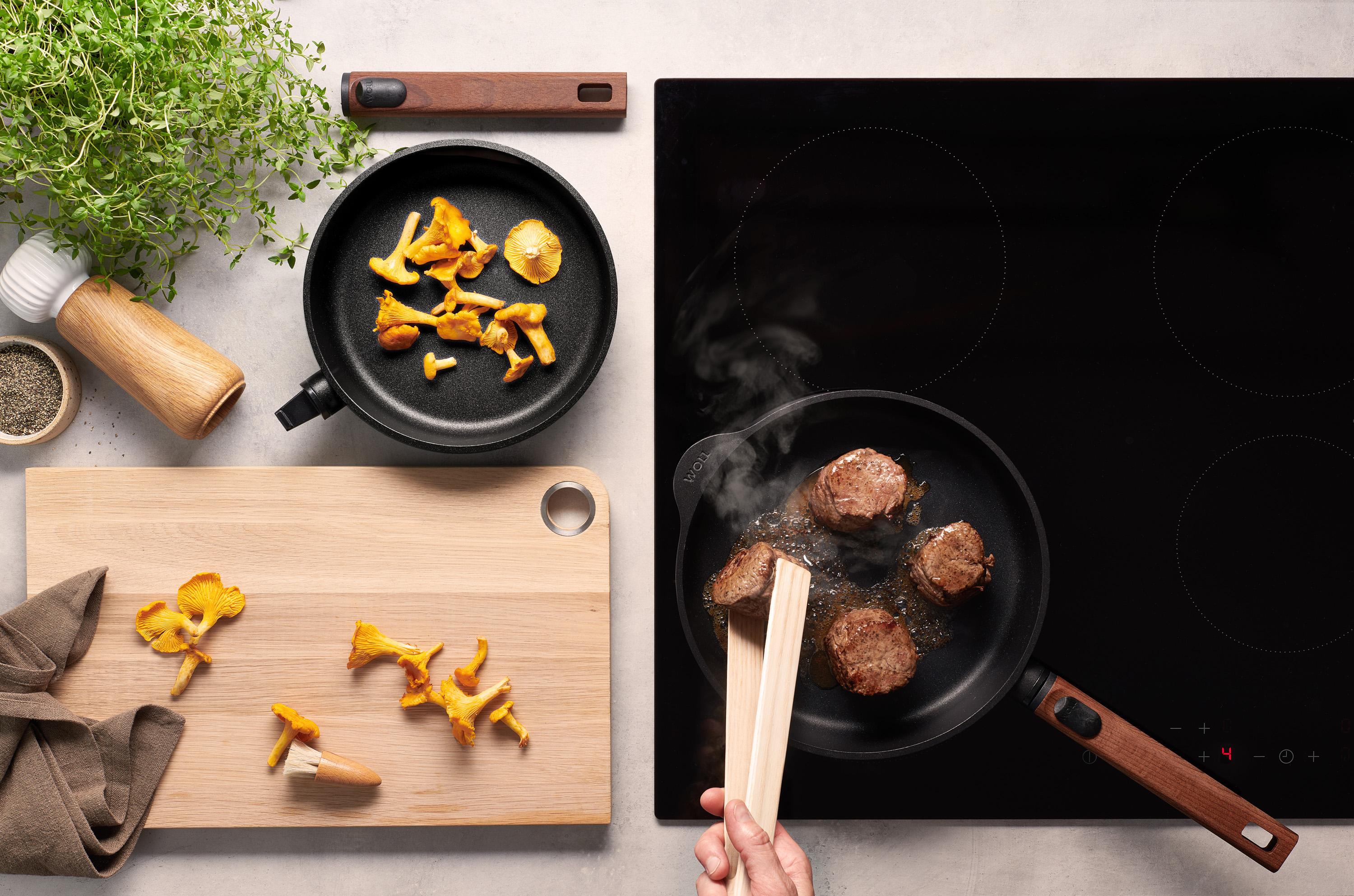 Eco Logic QXR Gusspfanne In einer runden Eco Logic QXR-Pfanne wird Fleisch angebraten und gewendet. In der Pfanne daneben liegen Pfifferlinge.