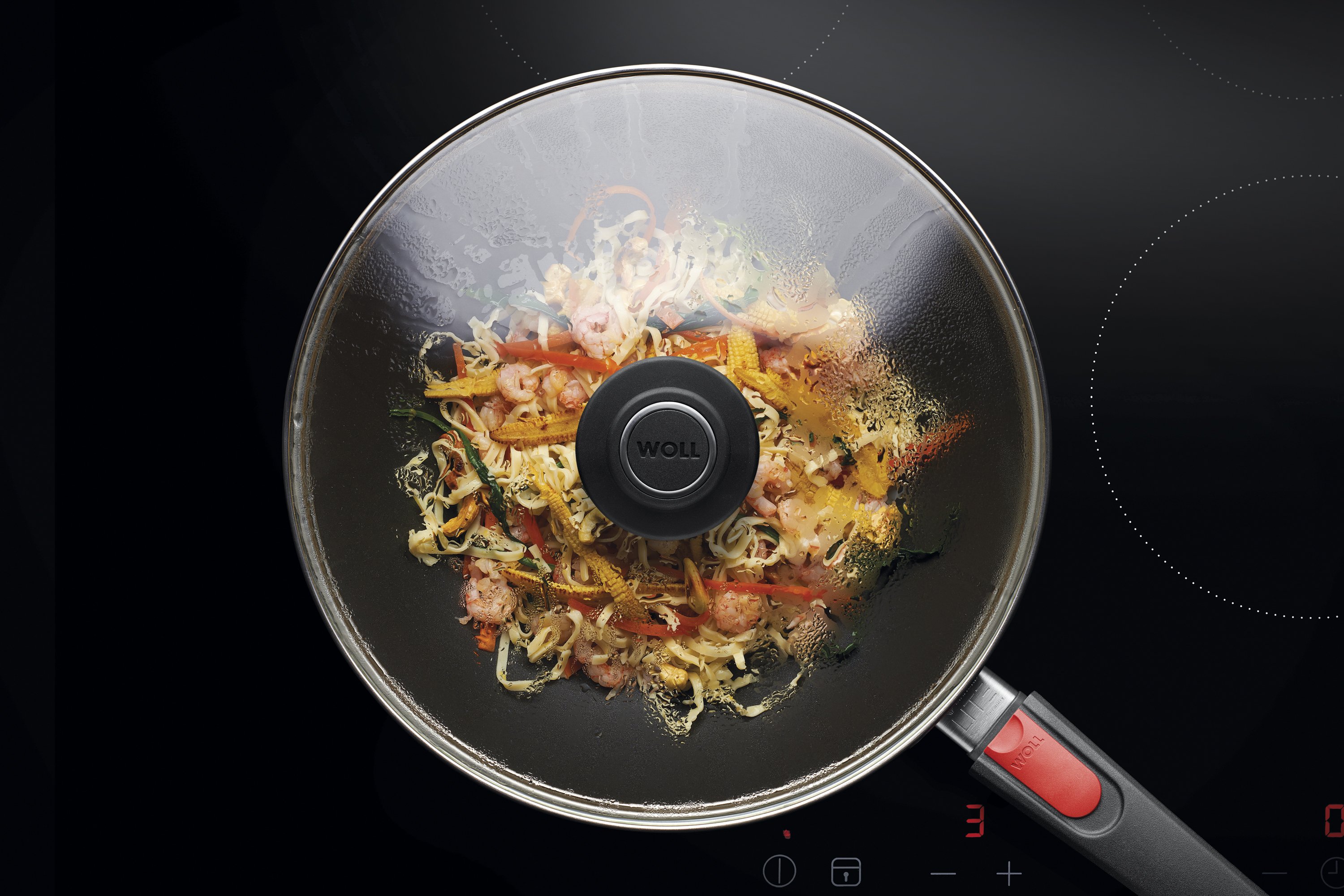 Sicherheitsglasdeckel, rund Auf dem Herd steht eine runde Diamond Lite Wok- und Rührpfanne In dieser befindet sich ein frisch zubereitetes Gericht. Am Glasdeckel hat sich Kondenswasser gebildet.