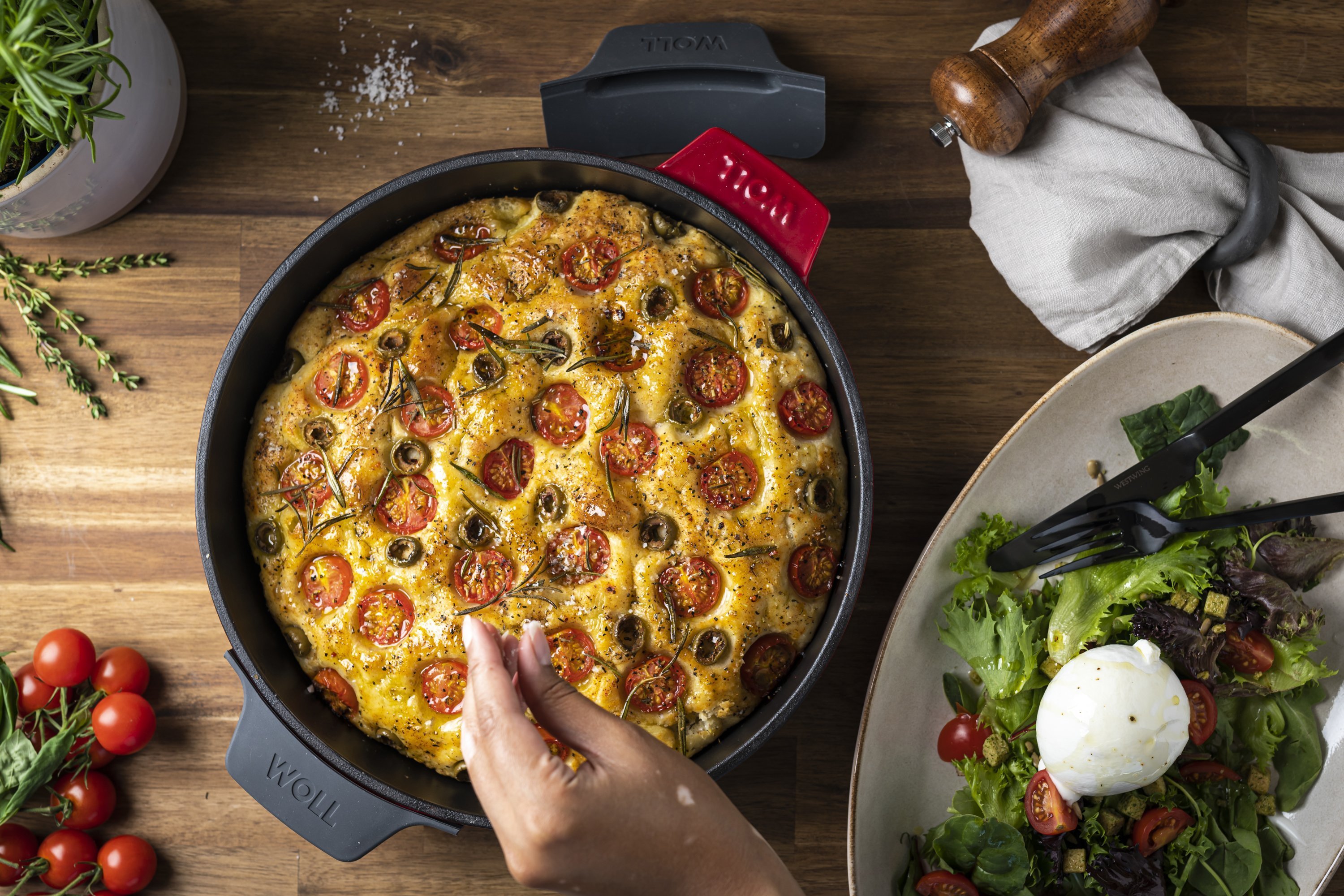 In einer runden, roten Iron Kasserolle befindet sich ein frisch gebackenes Focaccia, das mit Rosmarin und Meersalz garniert ist.