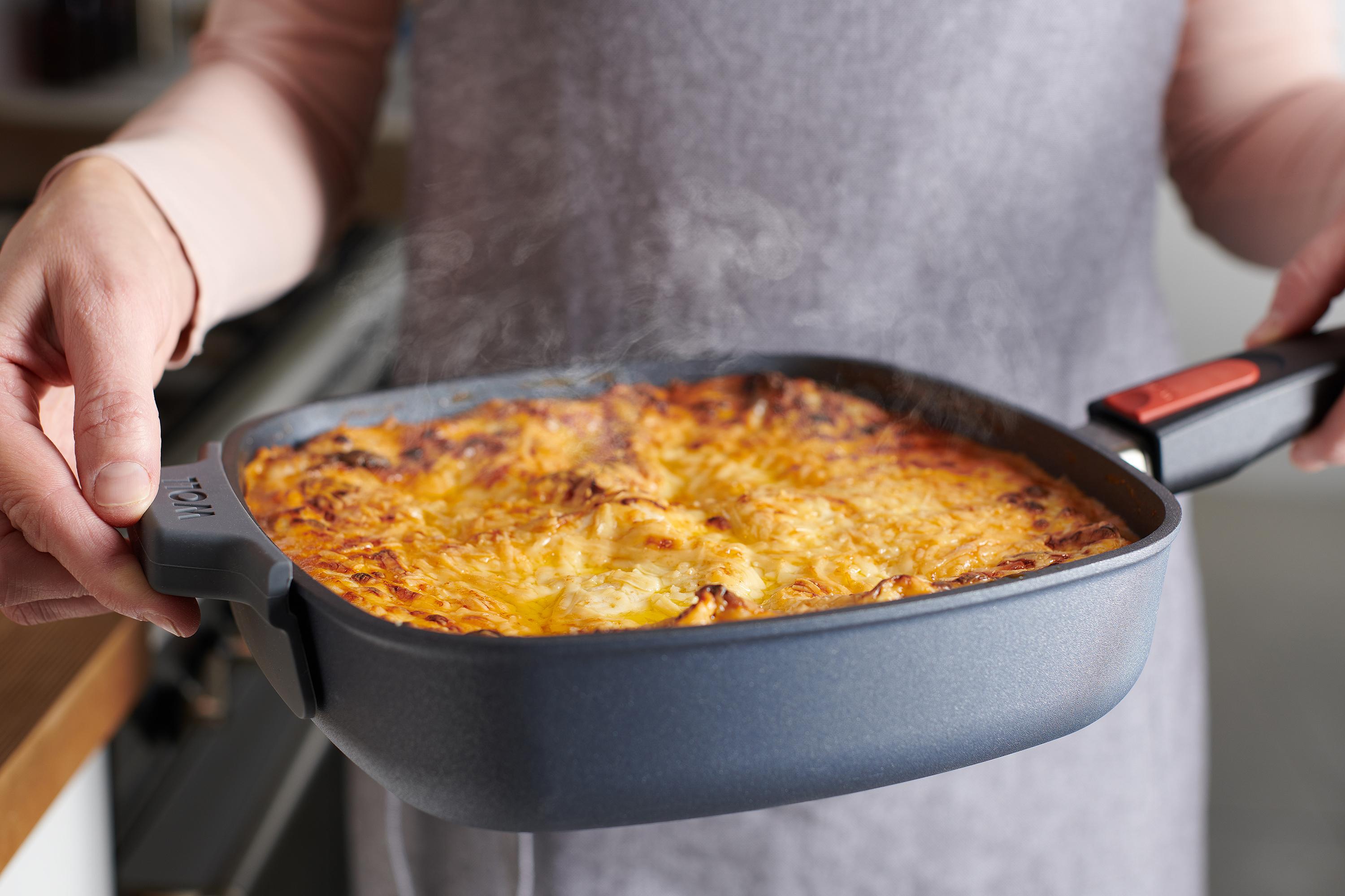 In einer viereckige Diamond Lite Pfanne befindet sich ein überbackenes Gericht und wird mit zwei Händen gehalten. Der Silikongriff schützt vor Hitze.