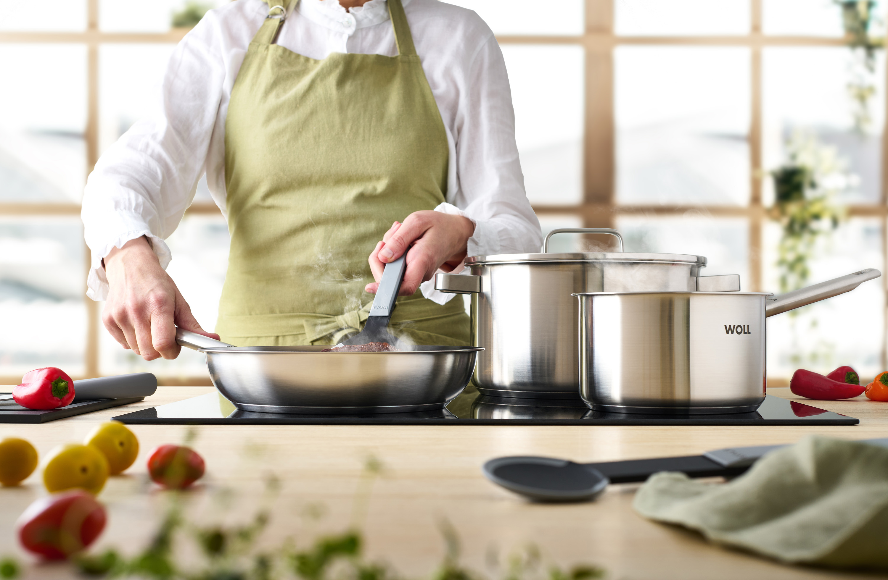 Steel Flachpfanne In einer Steel Pfanne wird Fleisch angebraten und gewendet. Zwei weitere Steel Töpfe stehen auf dem Herd.