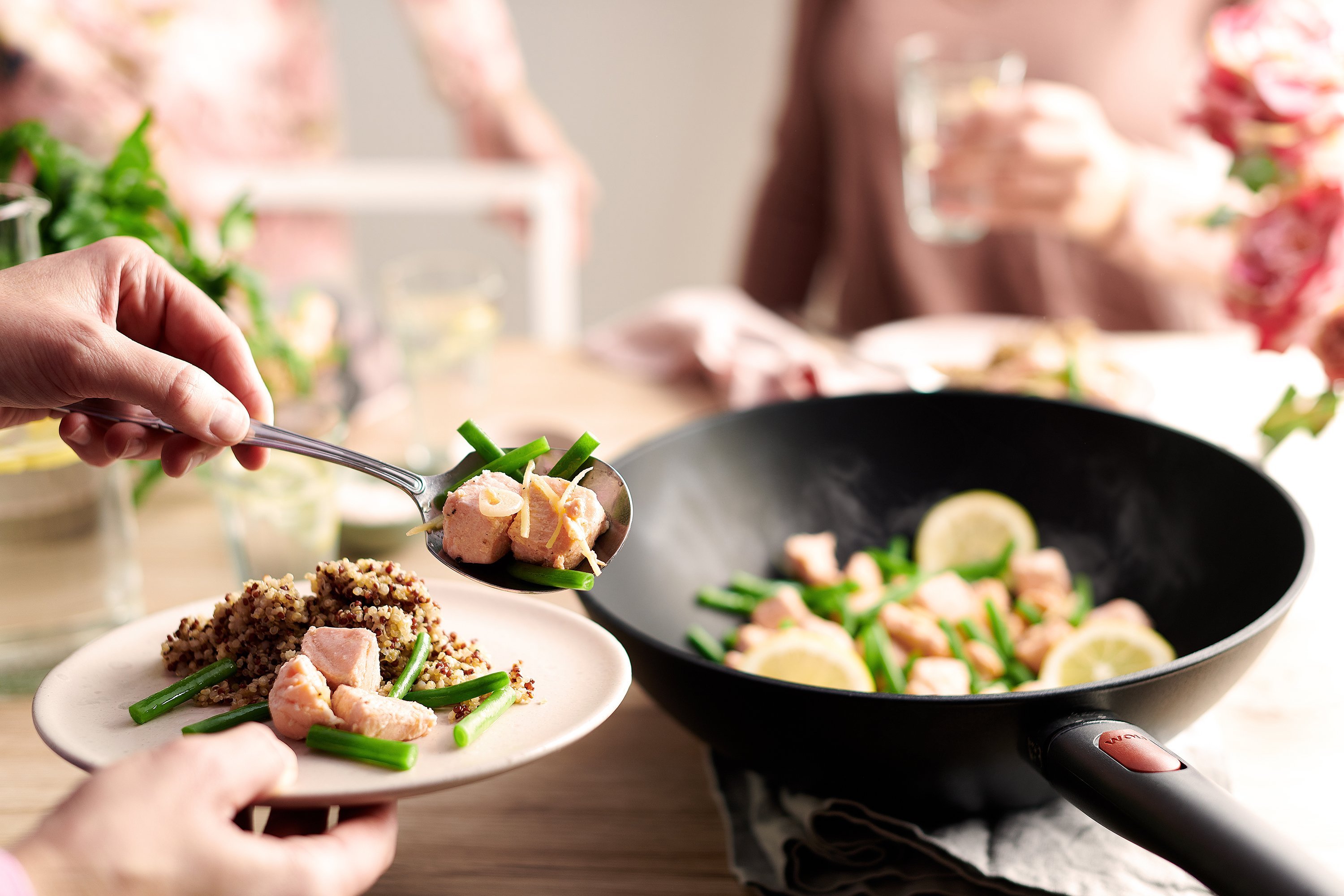 In einer runden Wok- und Rührpfanne der Serie Eco Lite QXR wurde frischer Lachs mit grünen Bohnen zubereitet. Anschließend wird eine Portion auf einen Teller gegeben.