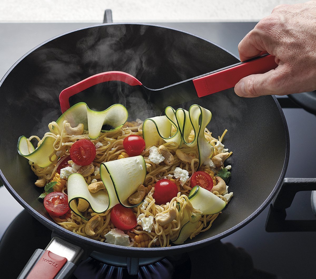 KU002_1200x1060_RGB In einer runden Diamond Lite Wok- und Rührpfanne wird ein Nudelgericht zubereitet, das mit einer roten Cock it Pfannenschaufel umgerührt wird.