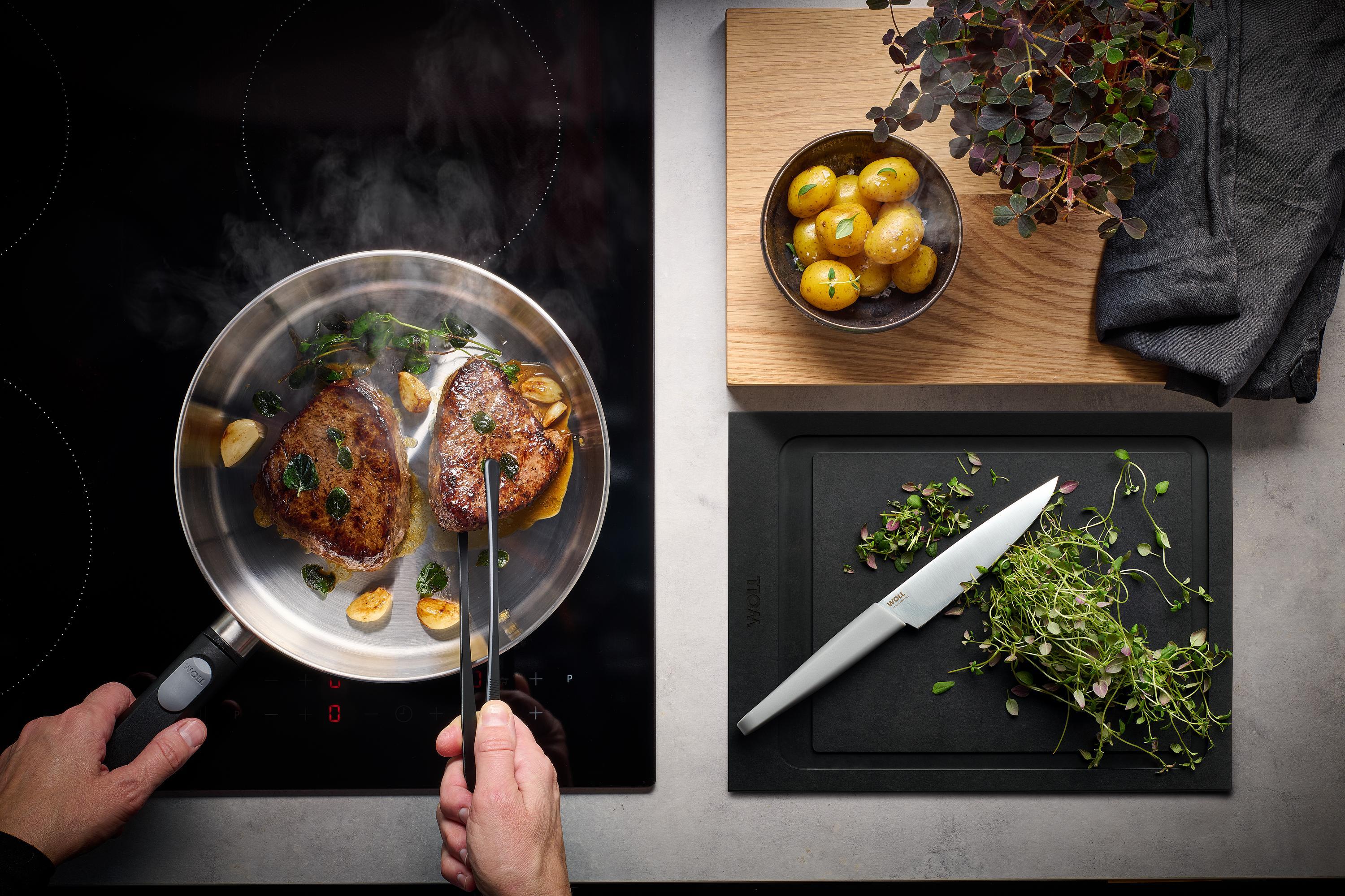 Logic Steel Flachpfanne Auf dem Herd steht eine runde Logic Steel Pfanne, in der Fleisch angebraten und gewendet wird.