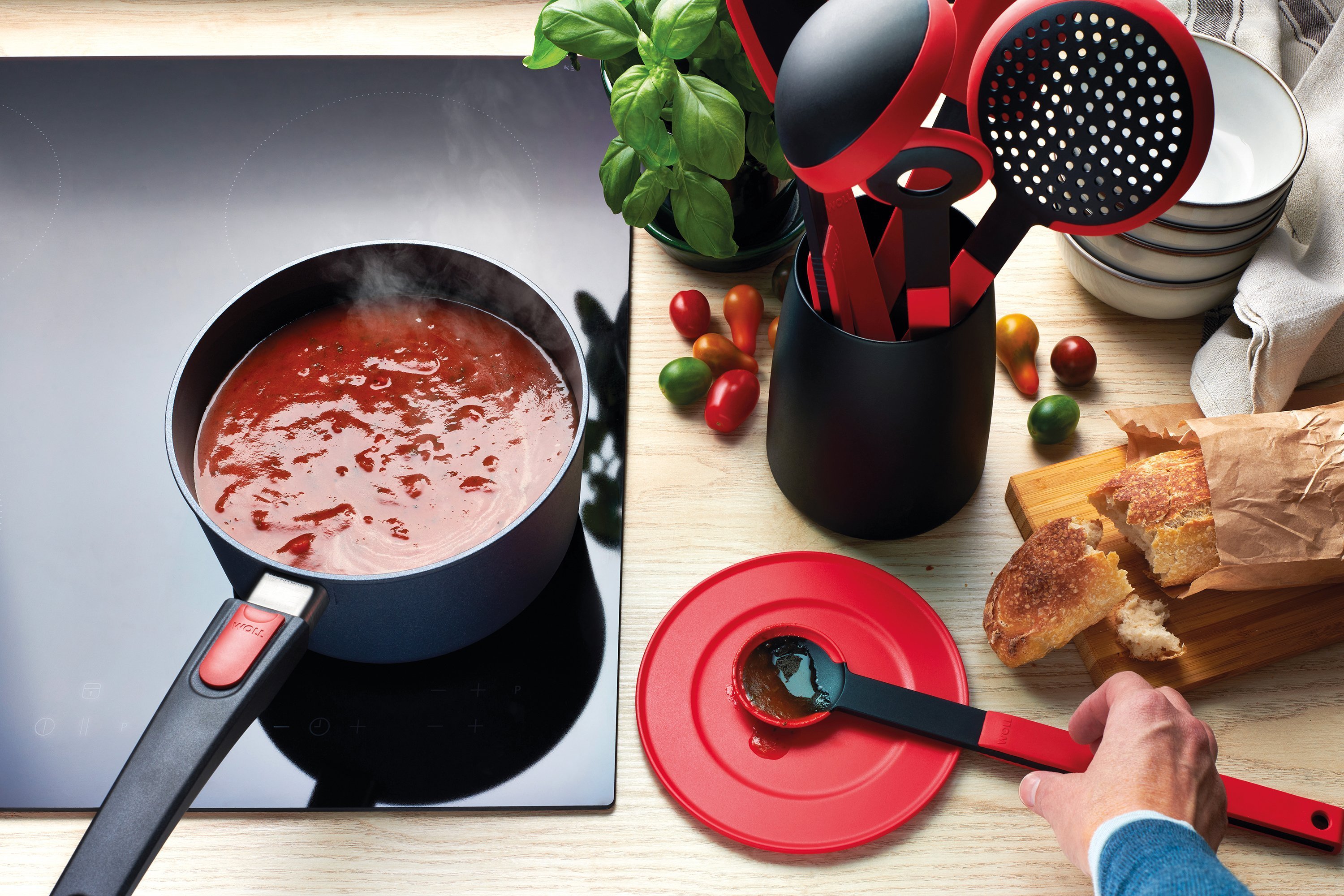 Cook it Küchenhelfer-Set mit Utensilienbehälter, 5-tlg. In einem runden Diamond Lite Stieltopf wird Tomatensoße gekocht. Auf der Arbeitsplatte liegen mehrere rote Cock it Küchenhelfer.