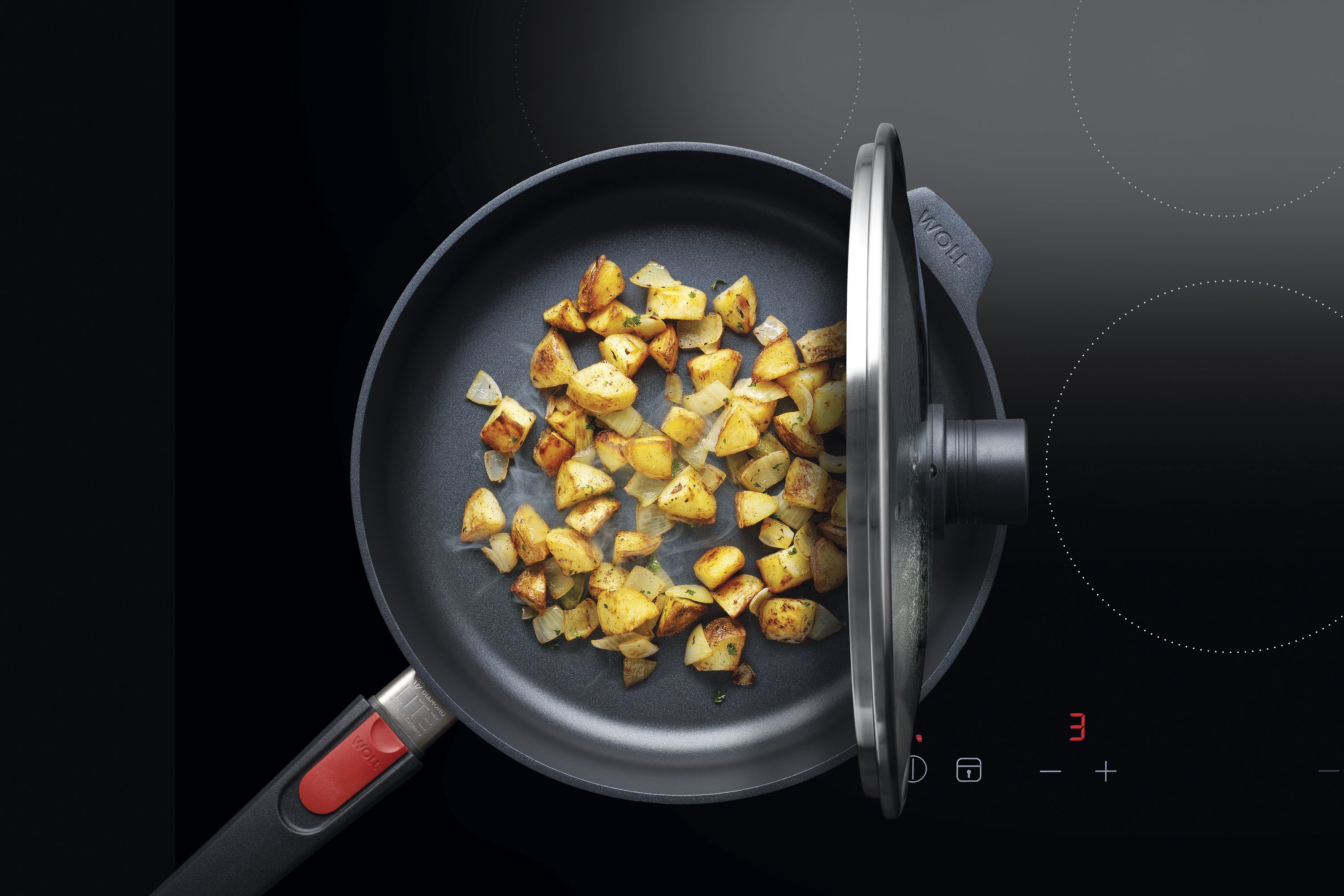 Auf dem Herd steht eine runde Diamond-Lite-Pfanne, in der ein Gericht zubereitet wird. Der Smart Lid steht auf der Pfannenkante.