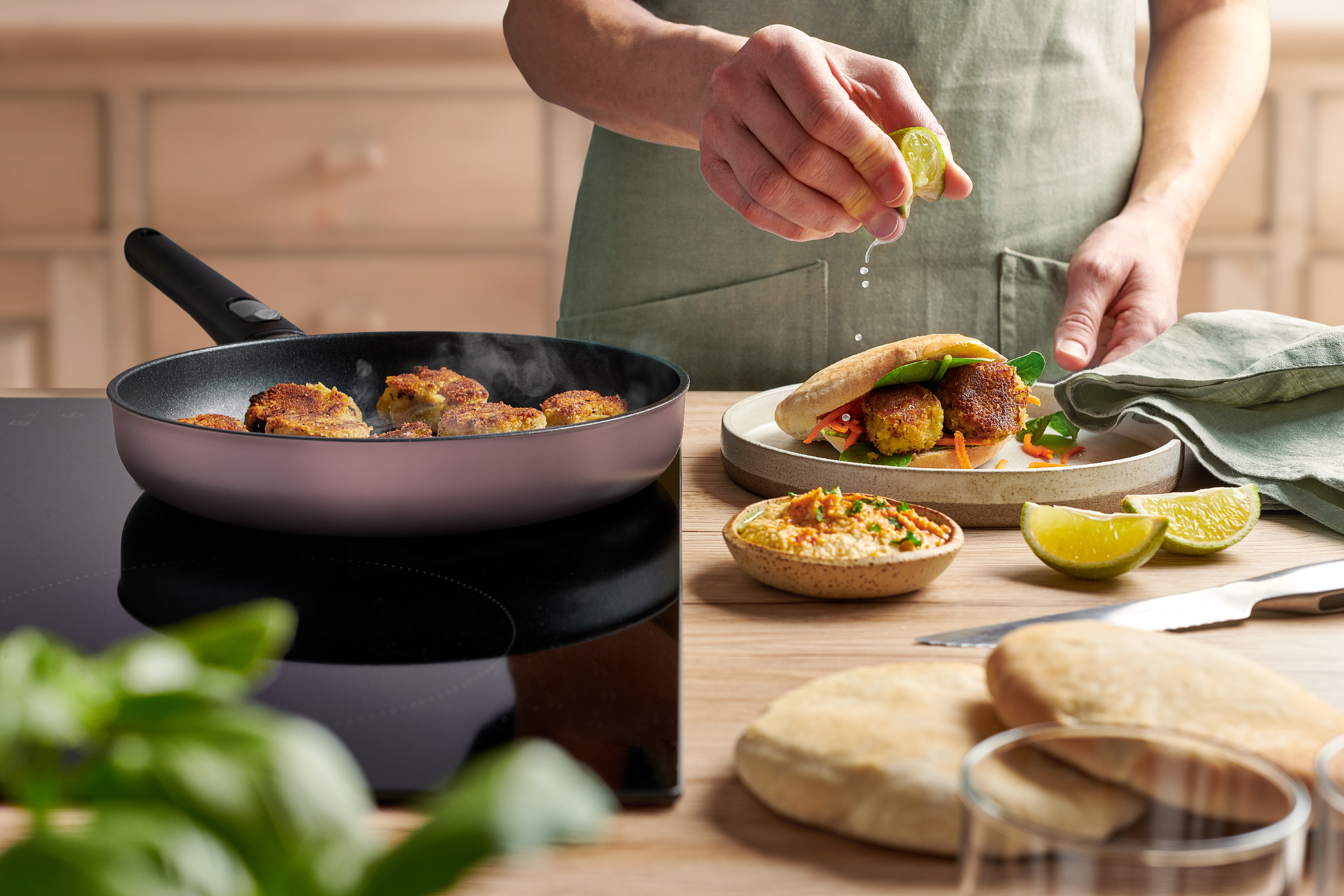 Ecolour Pfannen-Set, 2-tlg., Ø 28 + 24 cm In einer runden, hellrosa Ecolour Pfanne werden Falafel angebraten. Ein gefülltes Fladenbrot liegt auf einem Teller.