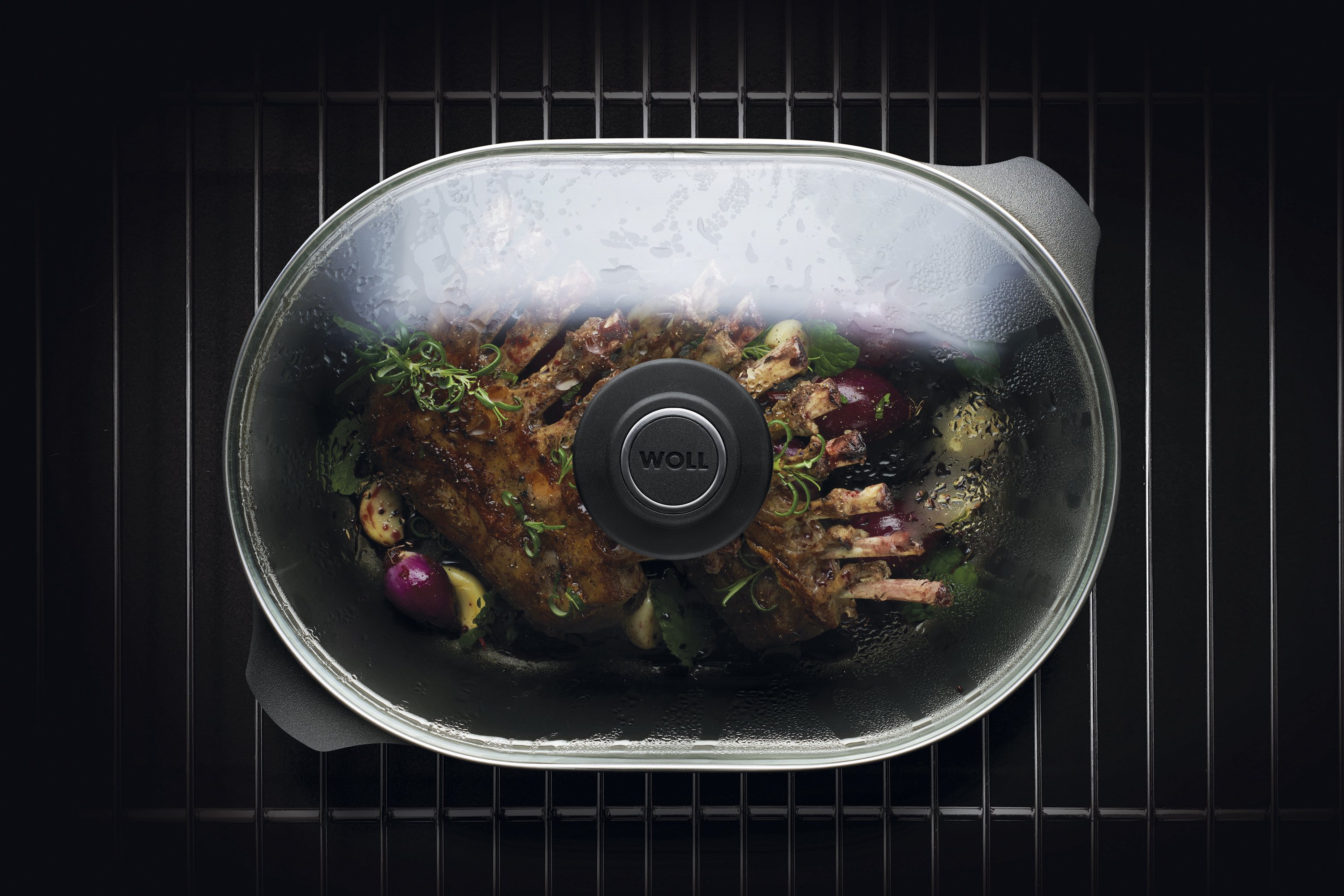 Auf dem Rost steht ein Titan Best Bräter mit Glasdeckel in der Fleisch zubereitet wird. 