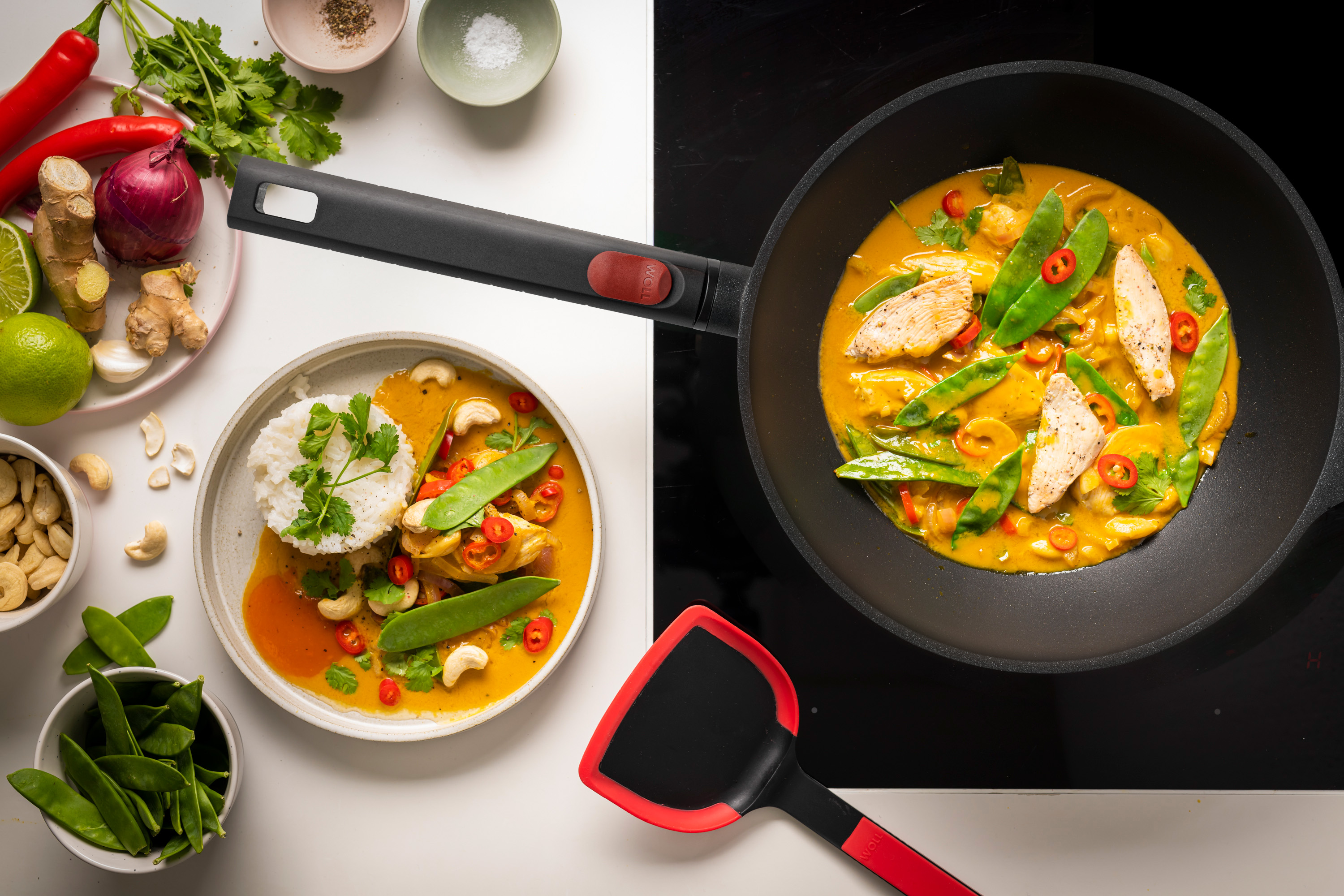 Auf dem Herd steht eine runde Logic XR Wok- und Rührpfanne, in der Curryhähnchen zubereitet wird.