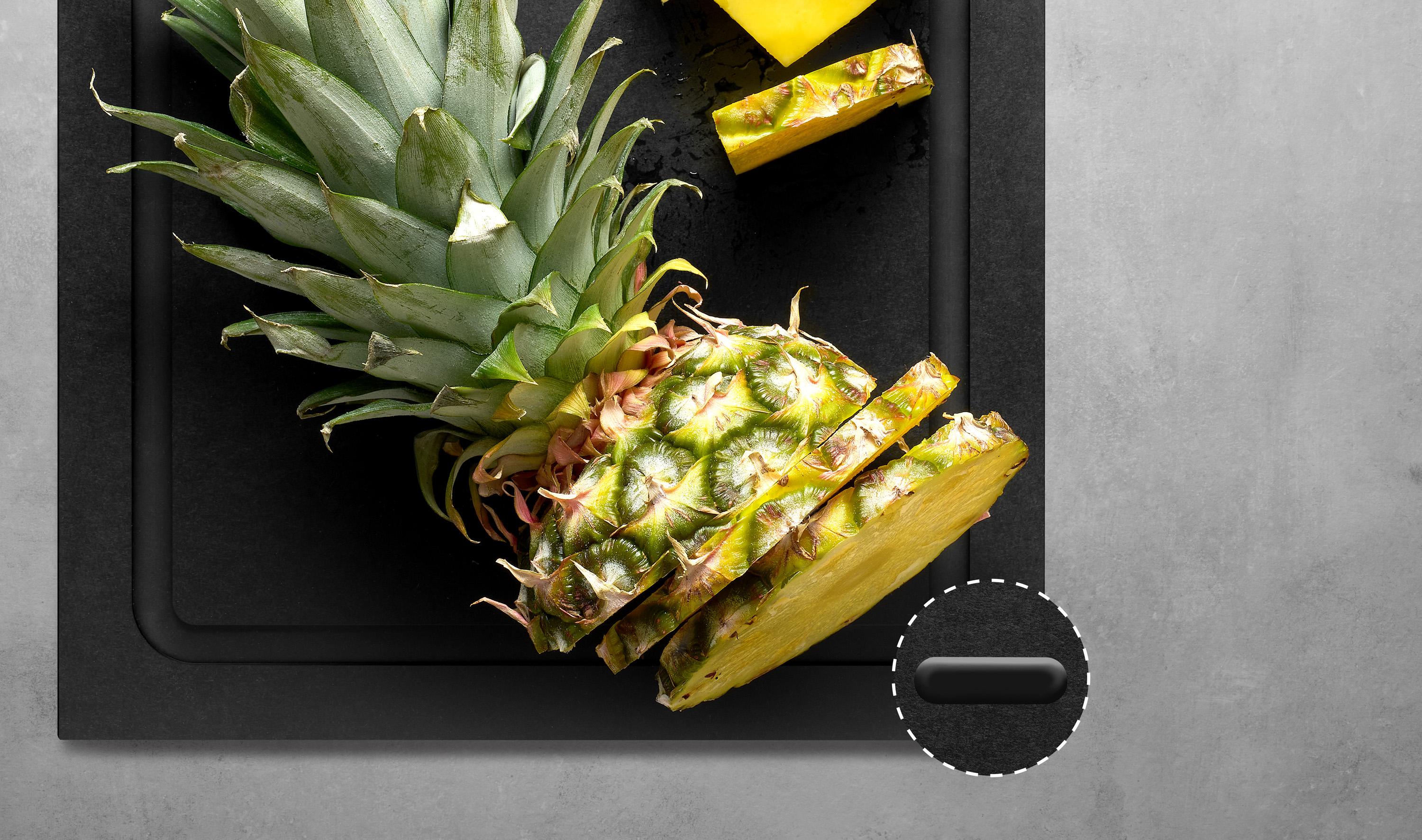 Auf dem Schneidebrett der Serie Cut & Serve mit Saftrinne liegt eine in Scheiben geschnittene Ananas. In einer Detailansicht sind die Silikonfüße auf der Unterseite zu sehen.