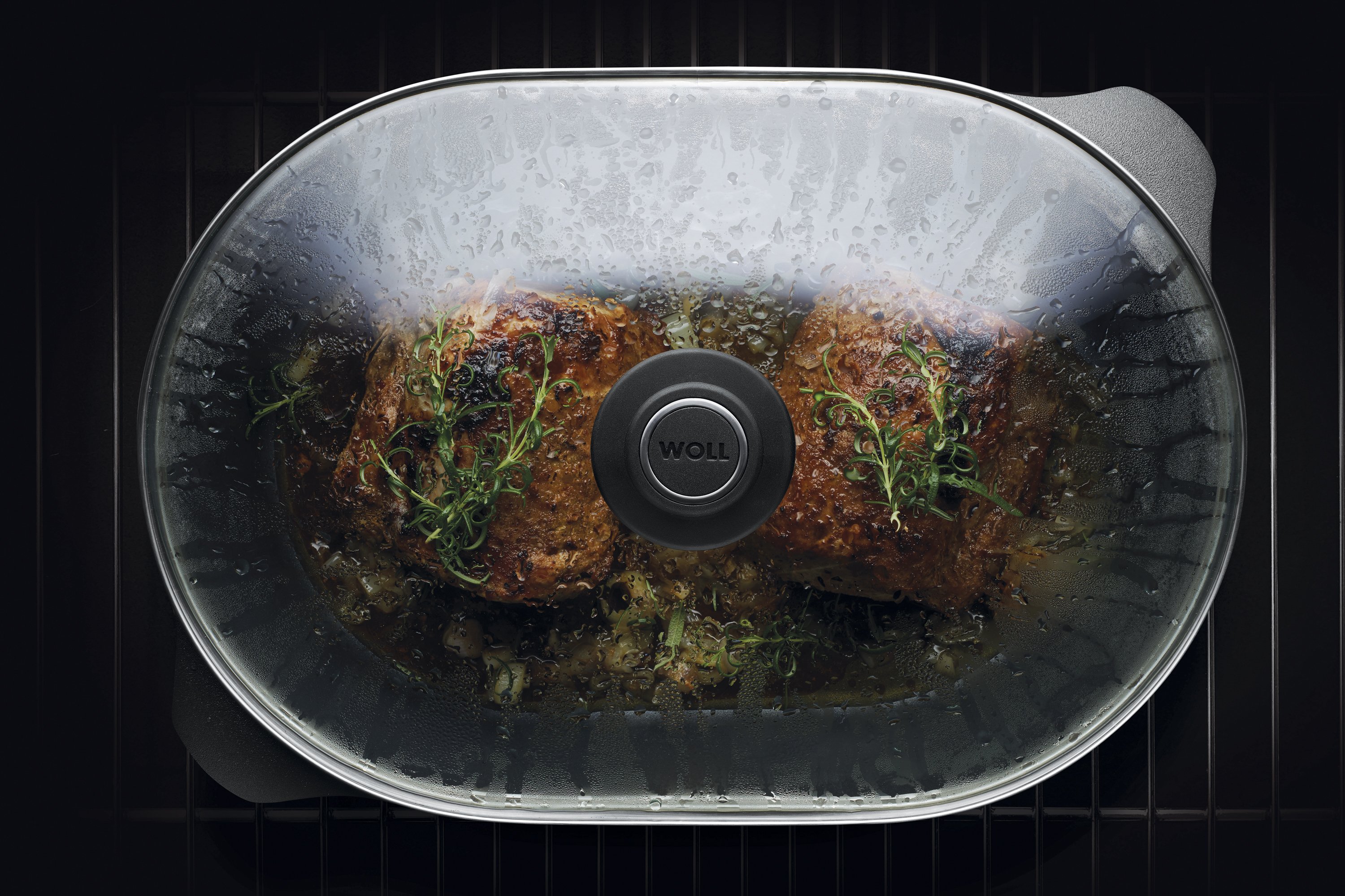 Auf dem Rost steht ein Titan Best Bräter mit Glasdeckel in der Fleisch zubereitet wird. 