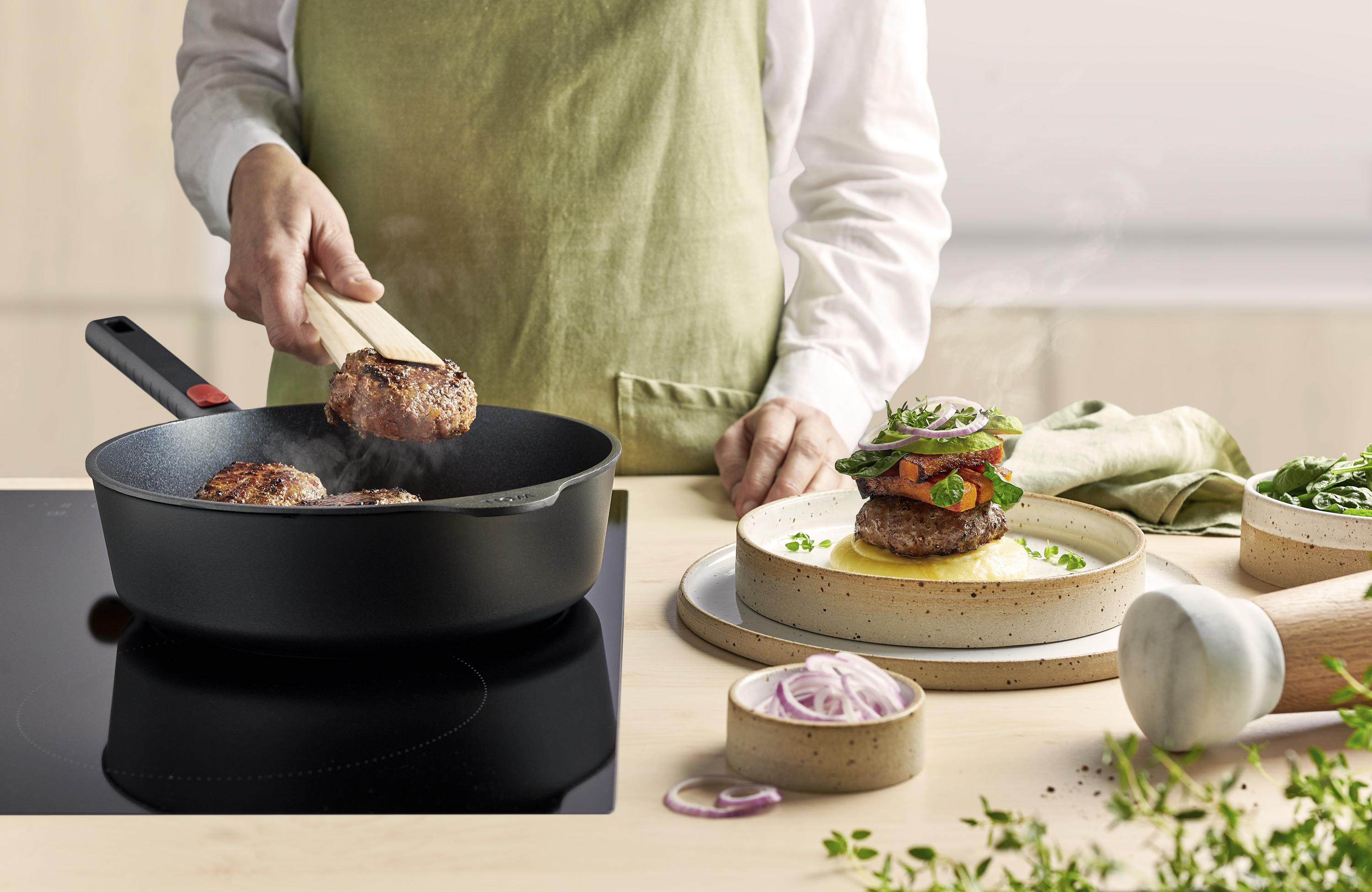 Eco Logic QXR Guss-Hochrandpfanne In einer runden Eco Logic QXR Pfanne werden Frikadellen angebraten und auf einem Teller platziert.