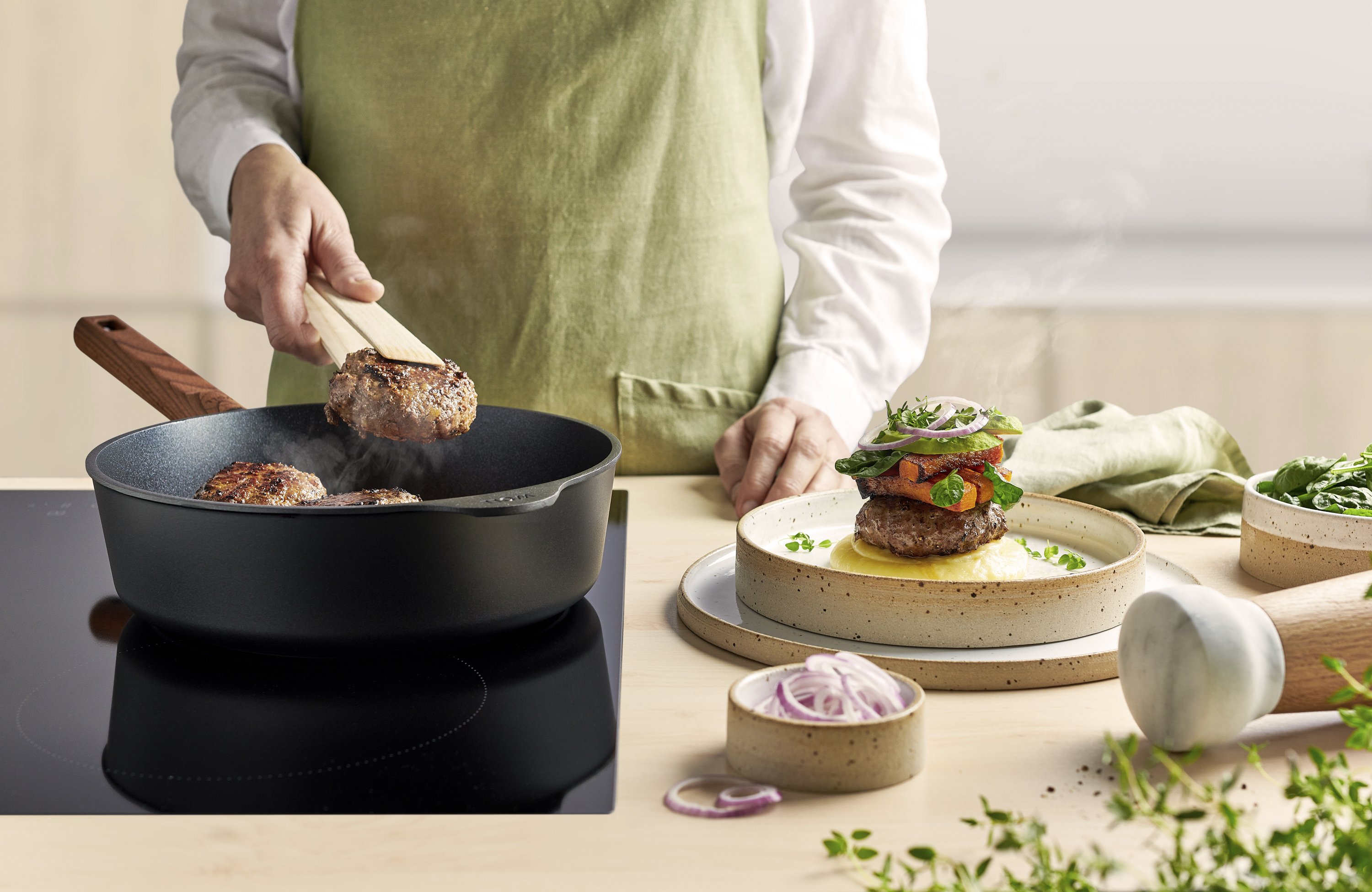 Eco Logic QXR Guss-Hochrandpfanne In einer runden Eco Logic QXR Pfanne werden Frikadellen angebraten und auf einem Teller platziert.