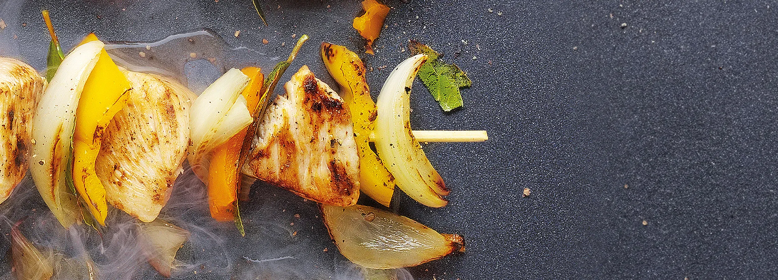 Detailaufnahme eines Spießes, der in der Pfanne angebraten wird.