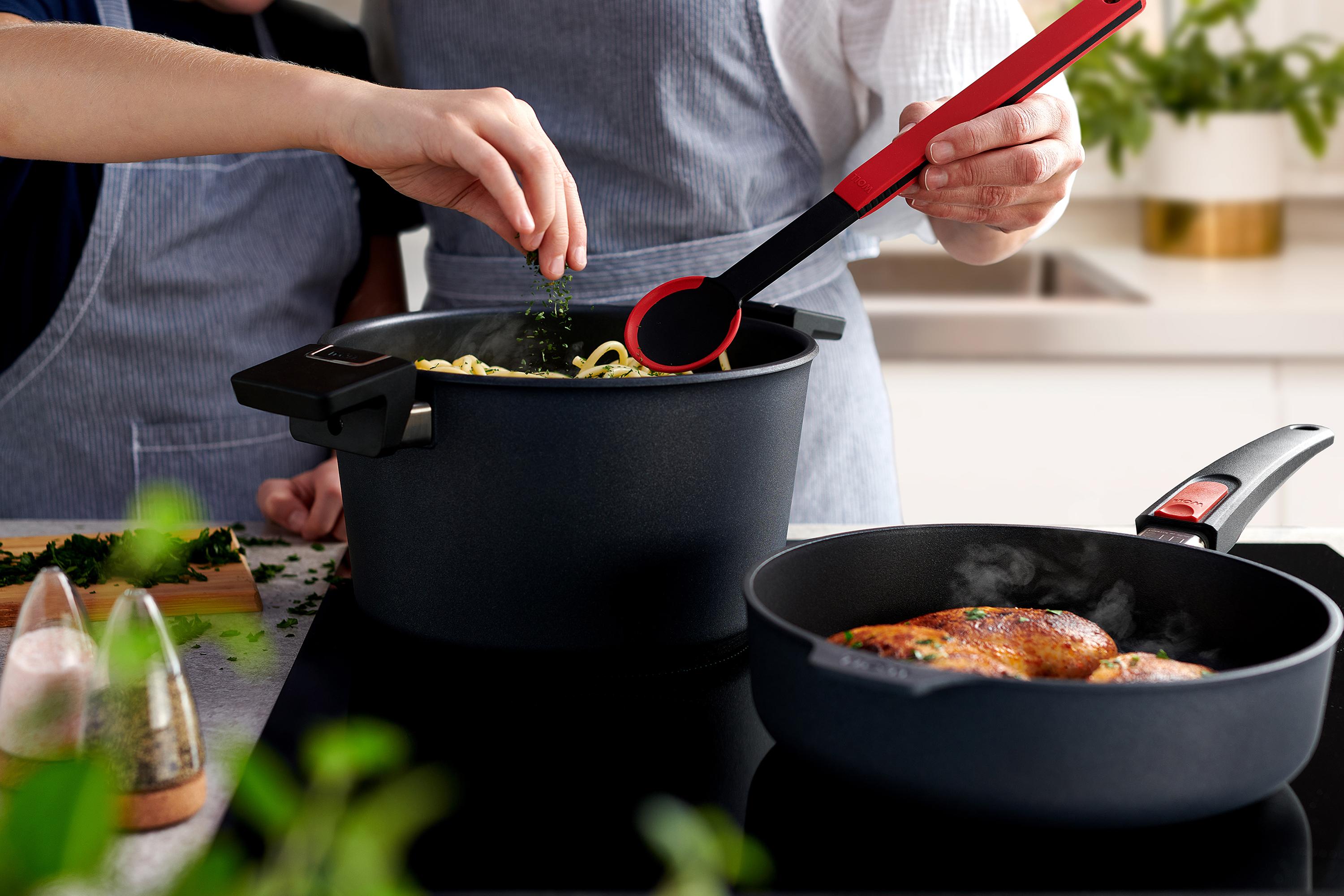 In einem runden Diamond-Lite-Topf werden Nudeln mit einem Cock-it-Kochlöffel umgerührt. Daneben steht eine runde Pfanne, in der Fleisch angebraten wird.