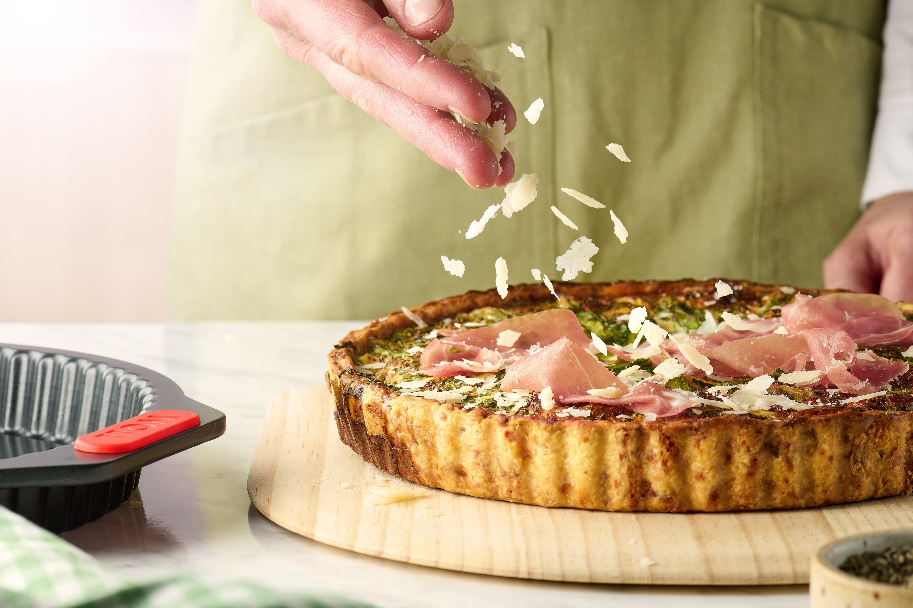 Let's bake! Quiche- und Tarteform mit Hebeboden Die gebackene Kartoffel Schinken Tarte liegt auf einem Brett. Die runde Let's bake! Quiche- und Tarteform steht daneben.