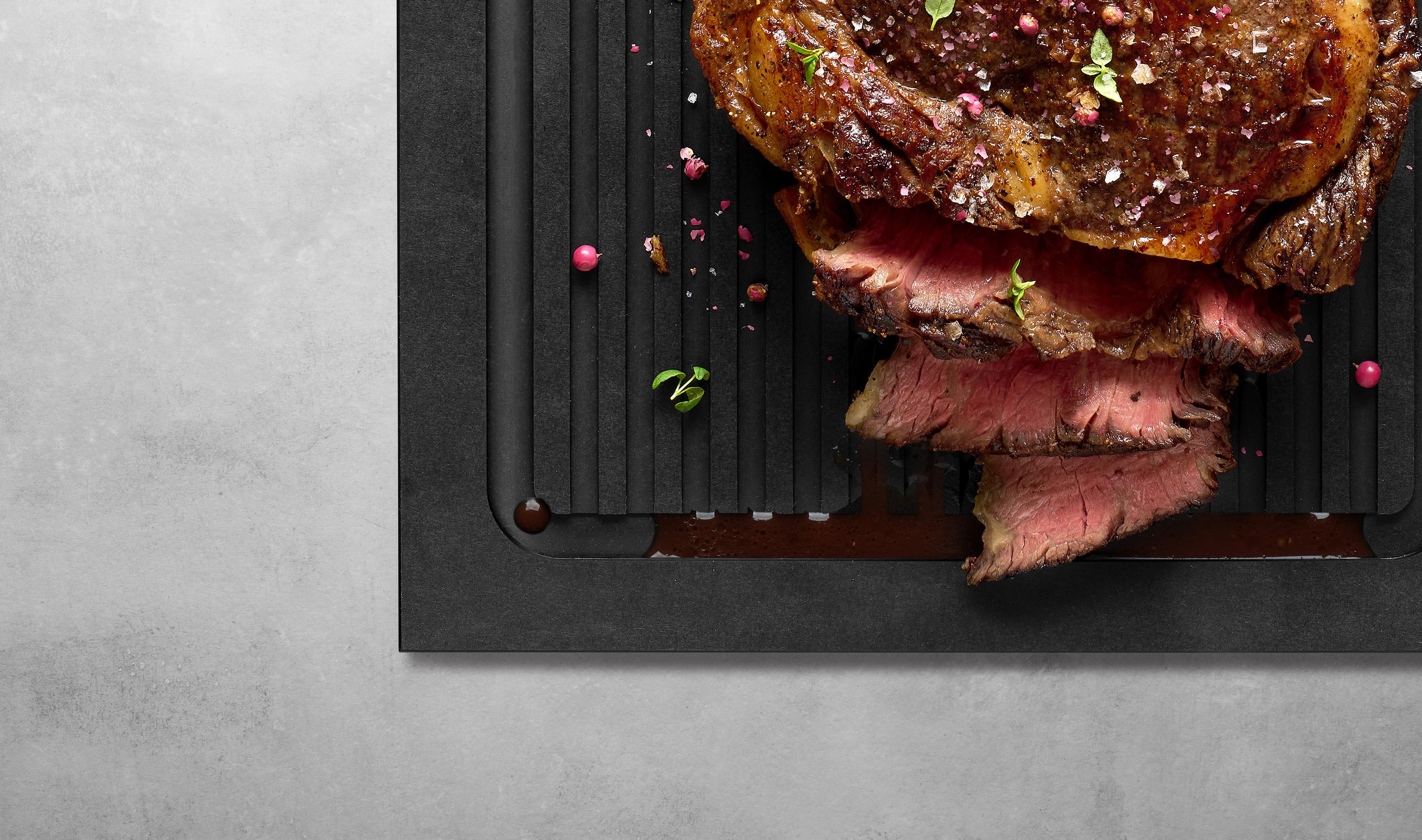 Cut & Serve Schneidebrett mit Griff und Rillen Ein Stück Fleisch wurde in Streifen geschnitten. Der dabei austretende Fleischsaft läuft in die Rillen des Cut & Serve Schneidebretts.