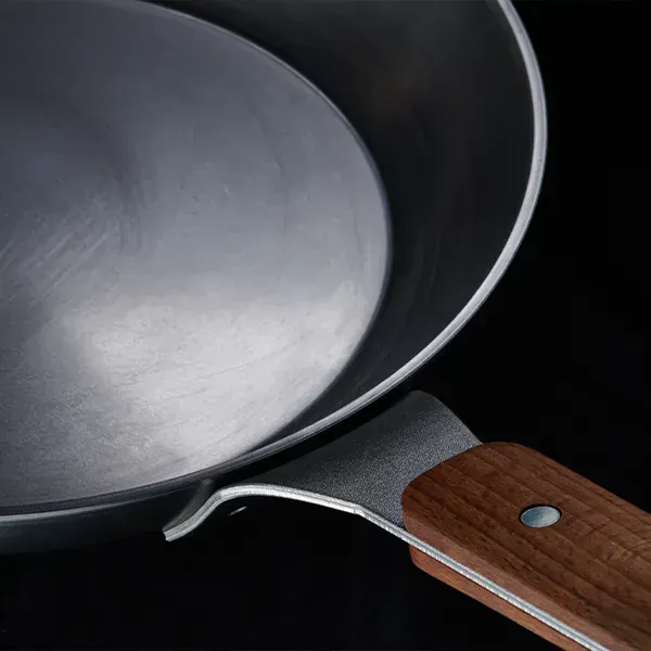 Eine Nahaufnahme zeigt eine runde Carbon Steel Pfanne, bei der man im Detail den festen Holzstiel erkennen kann.