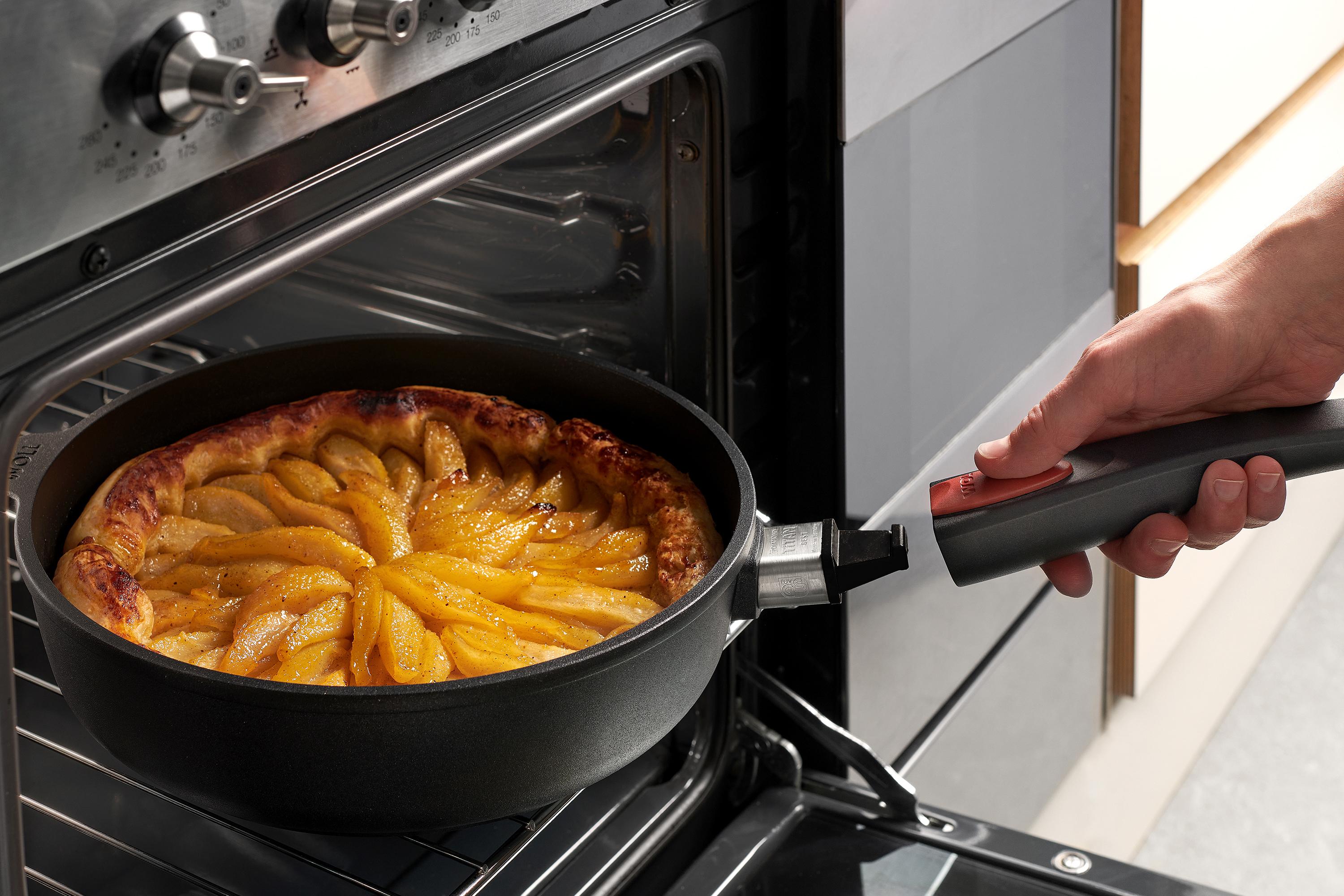 Titan Best Guss-Hochrandpfanne Auf dem Rost steht eine runde Titan-Best-Pfanne mit einem gebackenen Kuchen. Um die Pfanne aus dem Ofen zu entnehmen, wird der Stiel eingerastet.