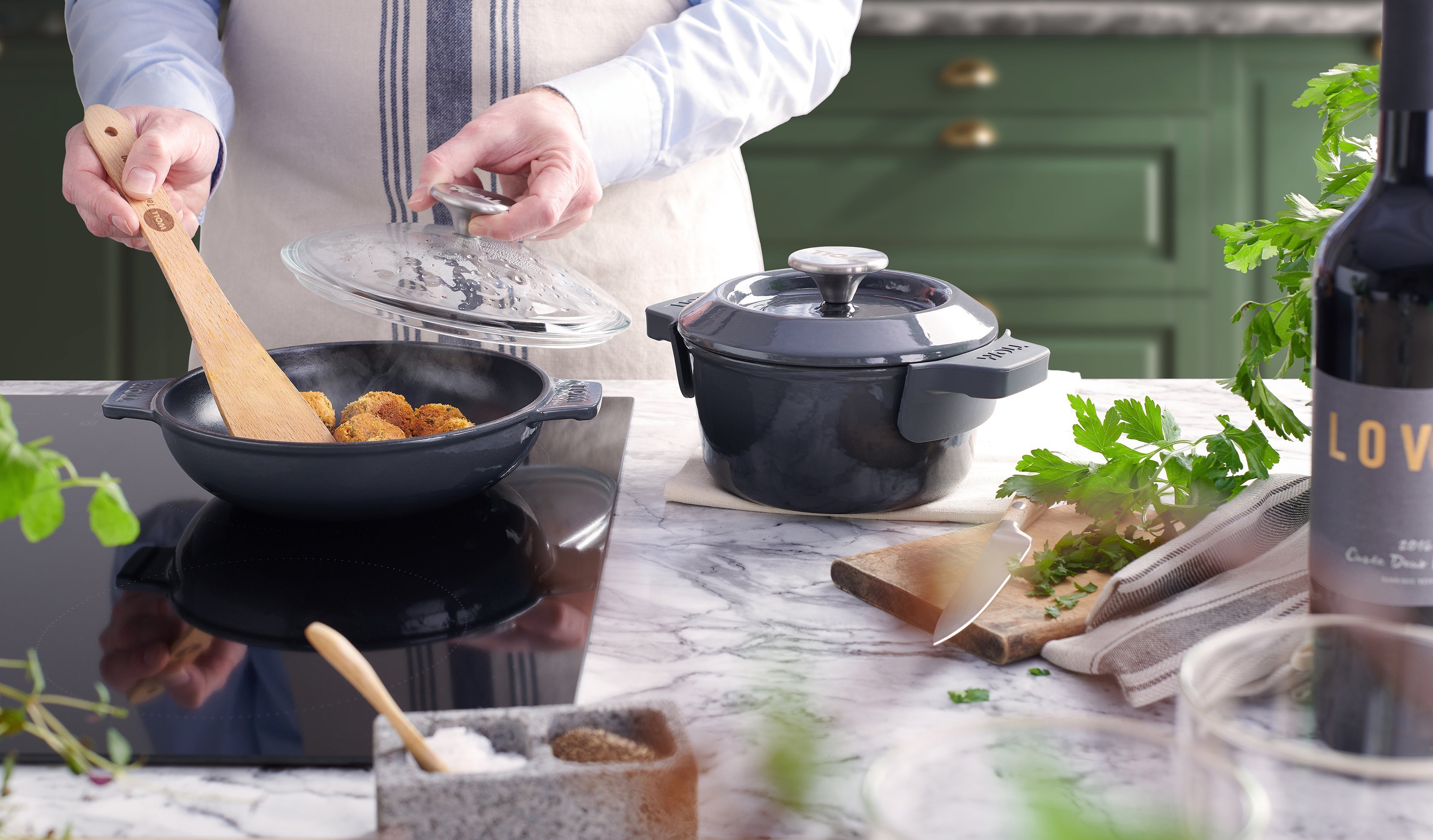 Auf dem Herd steht eine graue, runde Iron Servierpfanne, in der Falafel angebraten werden. Daneben steht ein Iron Topf mit Deckel.
