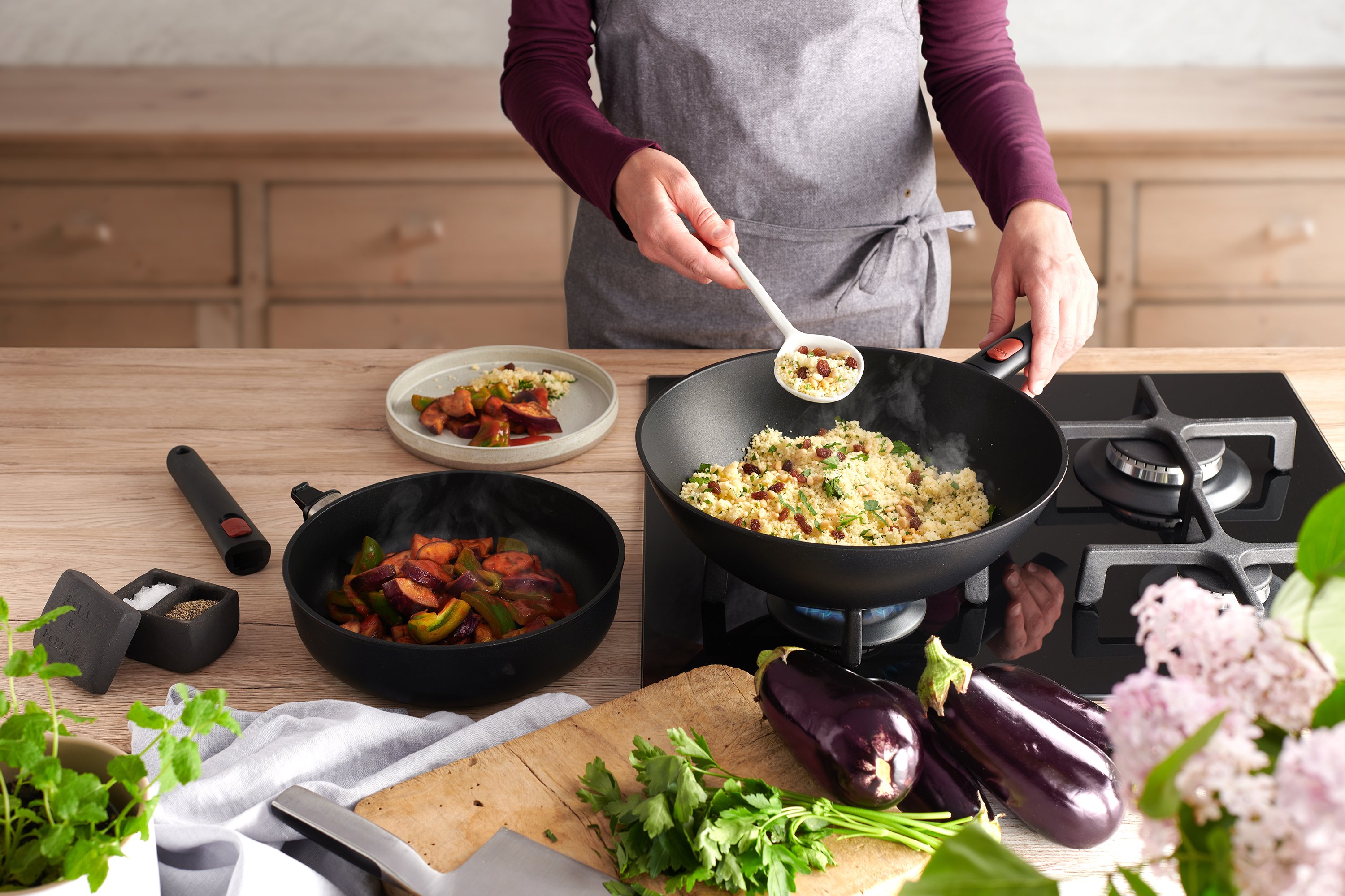 11030ELI-1728ELI_3000x2000px_RGB_WebuGAC1yWSHiQJH In einem runden Eco Lite Wok wird Couscous Salat zubereitet. Daneben steht eine weitere Eco Lite Pfanne mit Gemüse.