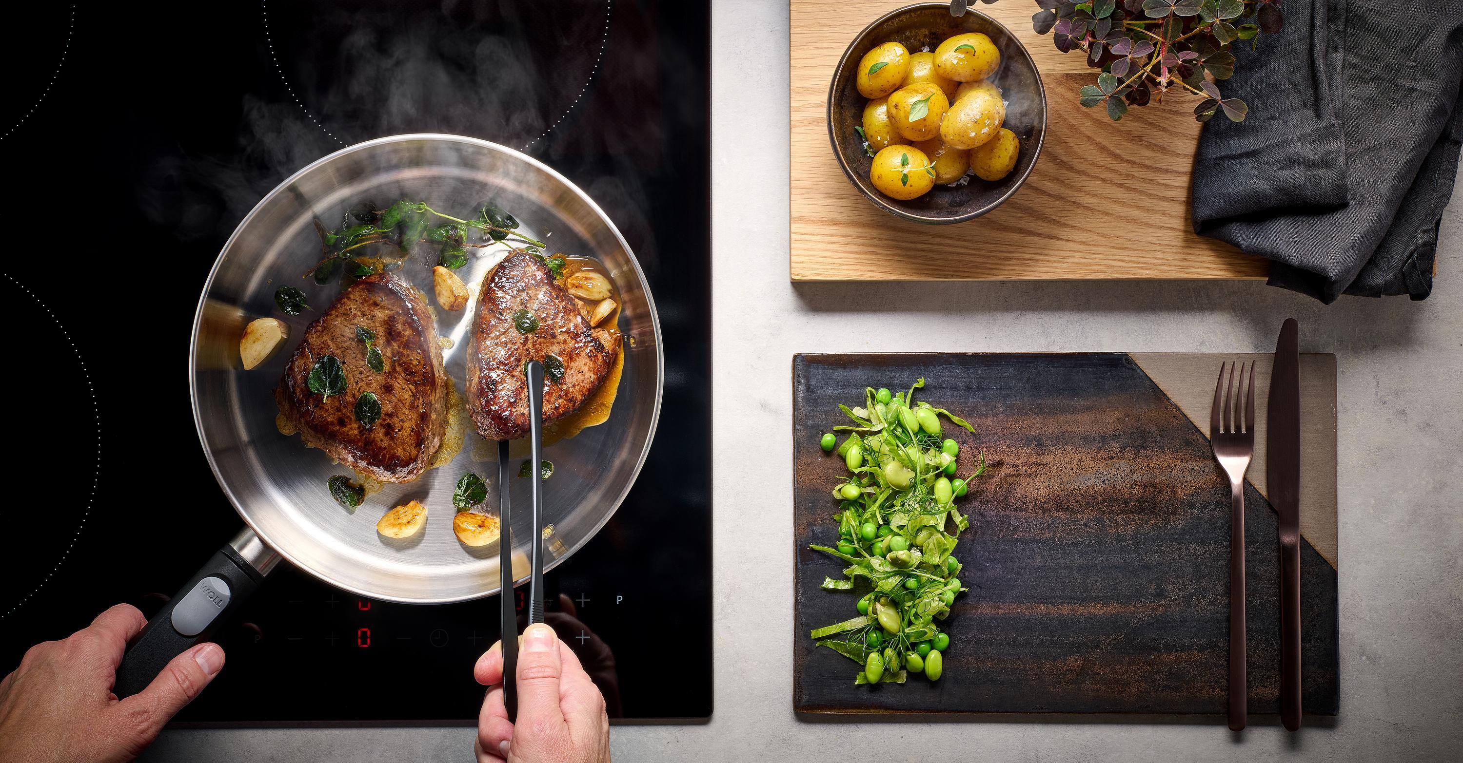 Logic Steel Flachpfanne Auf dem Herd steht eine runde Logic Steel Pfanne, in der Fleisch angebraten und gewendet wird.