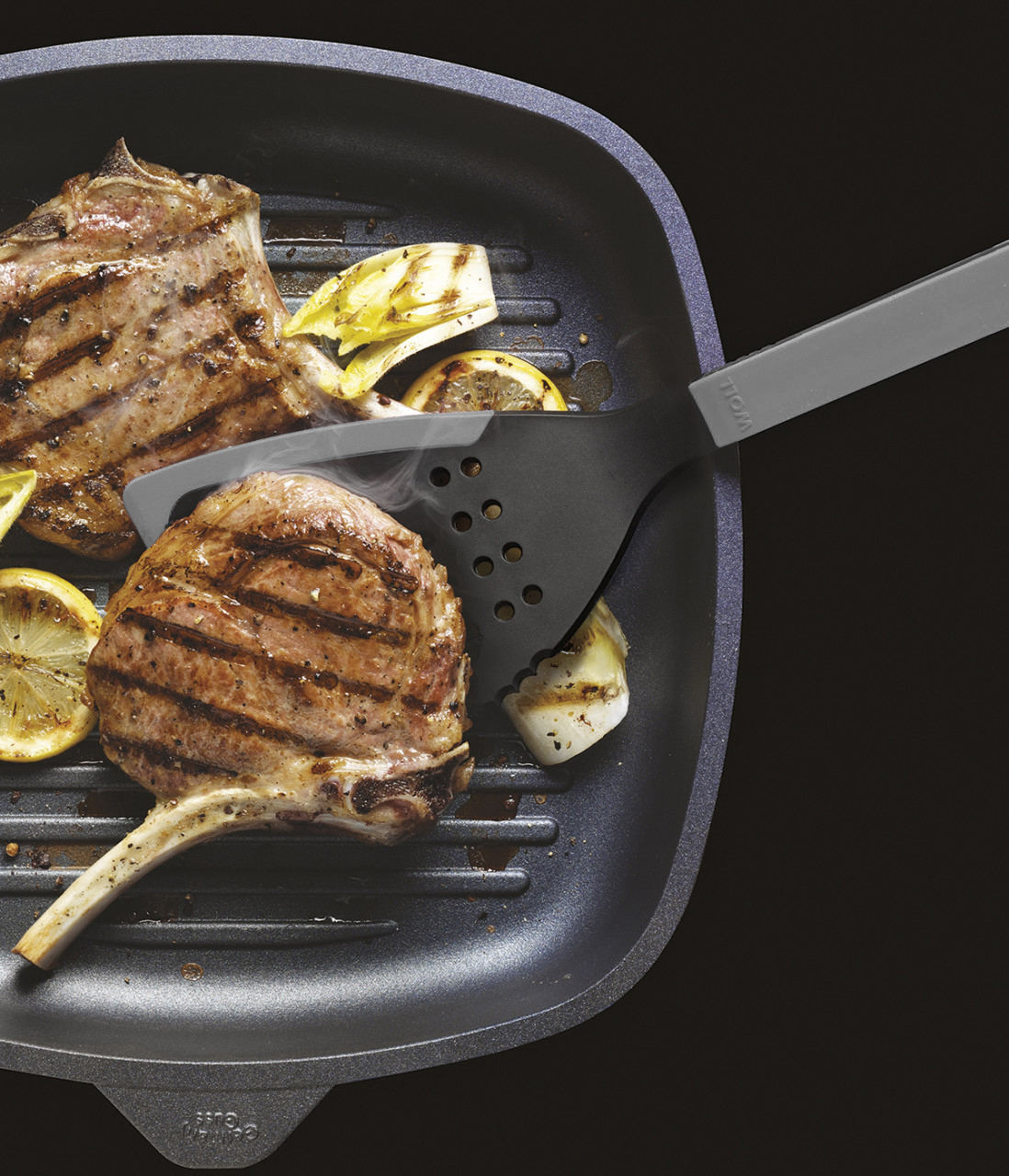 Cook it Jumbo-Pfannenwender In einer viereckigen Grillpfanne werden zwei Fleischstücke angebraten und mit einem grauen Cock it Jumbo Pfannenwender gewendet.