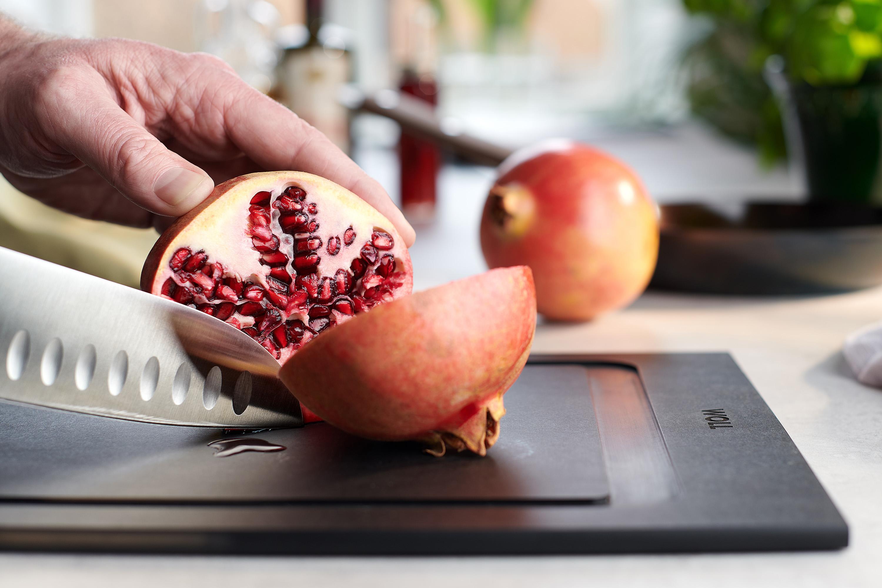 Cut & Serve Schneidebrett Ein Granatapfel wird auf einem Cut & Serve Schneidebrett mit einem Messer geteilt.