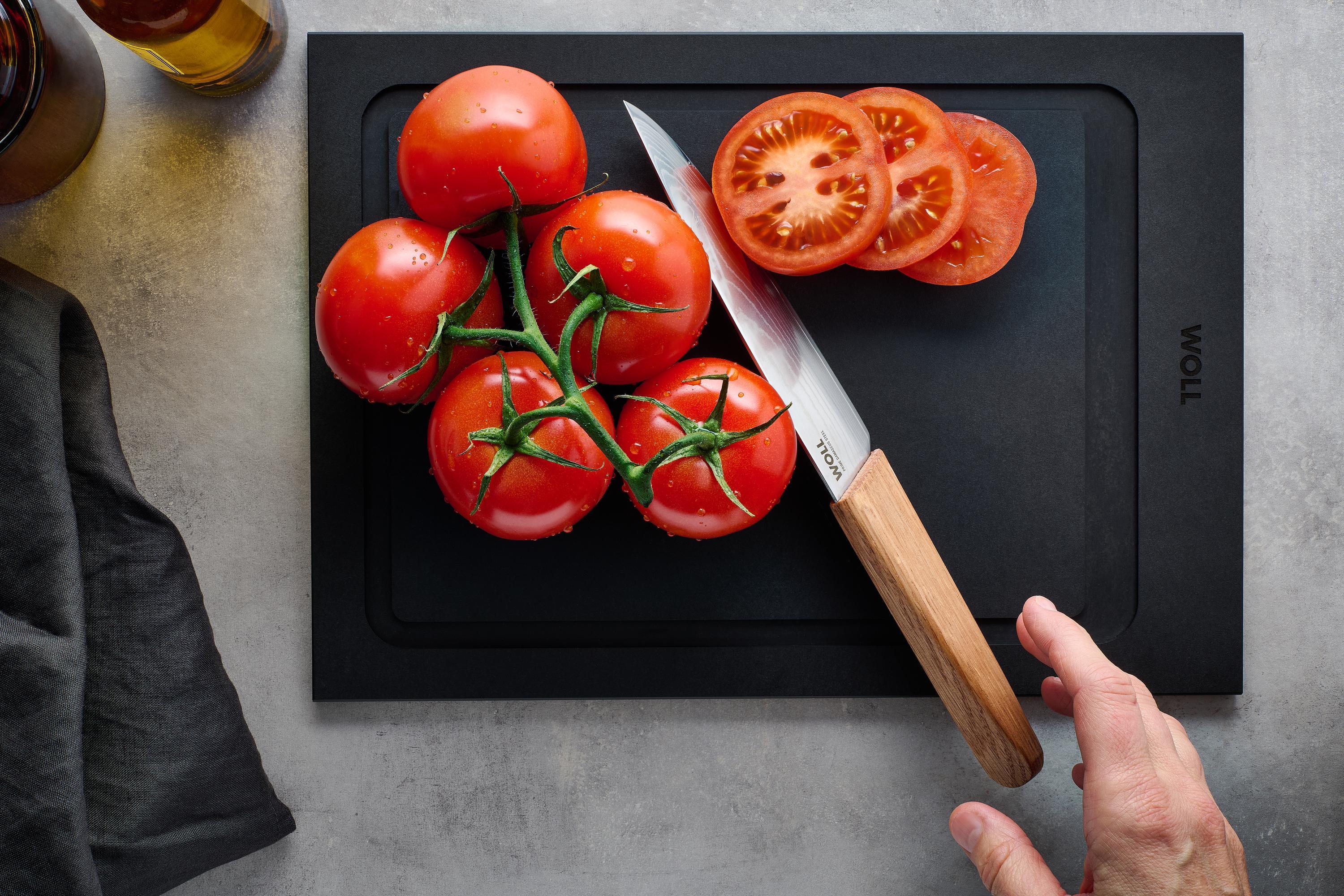 Prime Edge Kochmesser Kompakt Mit dem Prime Edge Kochmesser Kompakt wird eine Tomate auf einem Schneidebrett in Scheiben geschnitten.